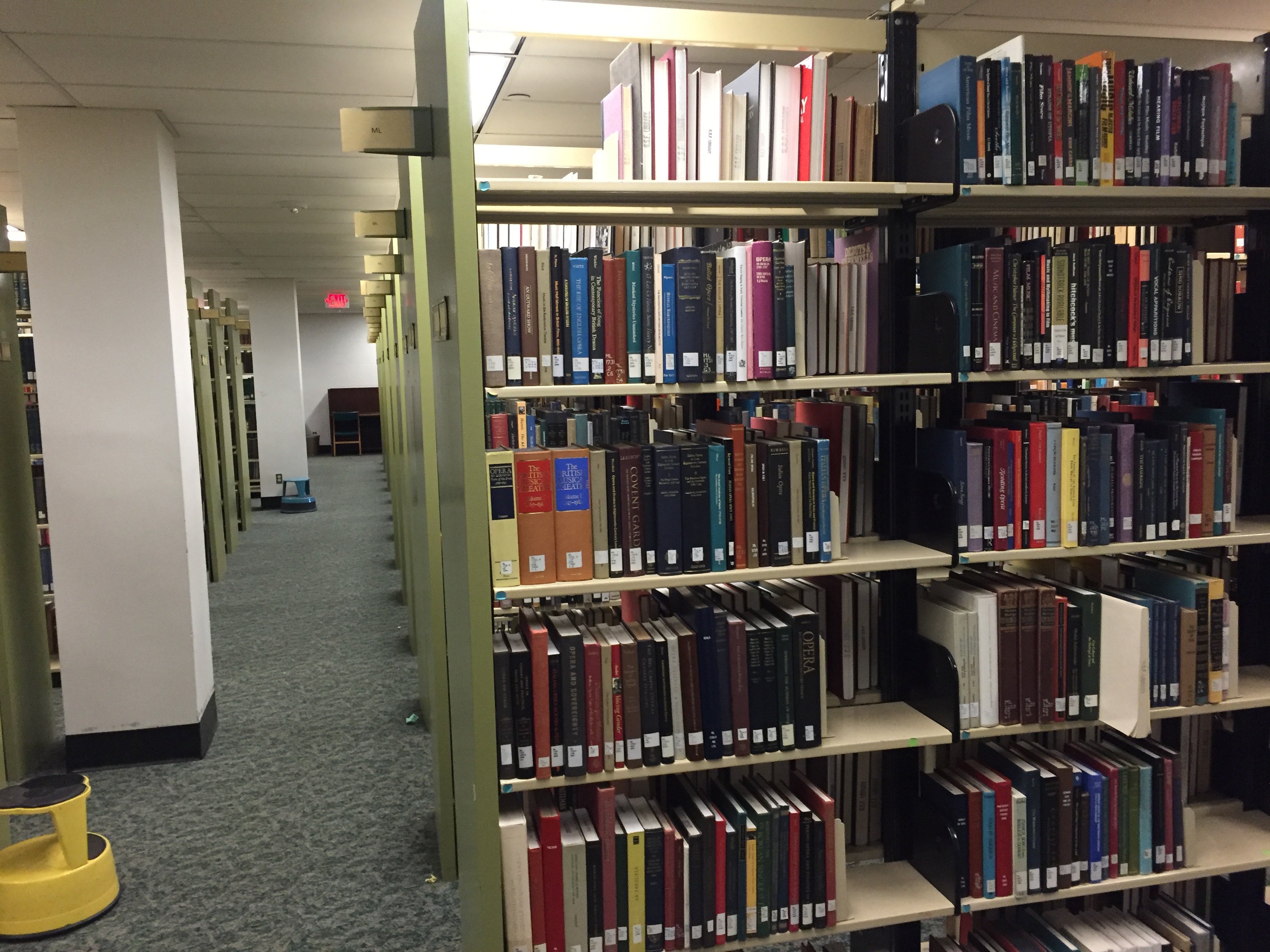 Rows of metal bookshelves filled with books inside a library under fluorescent lighting.