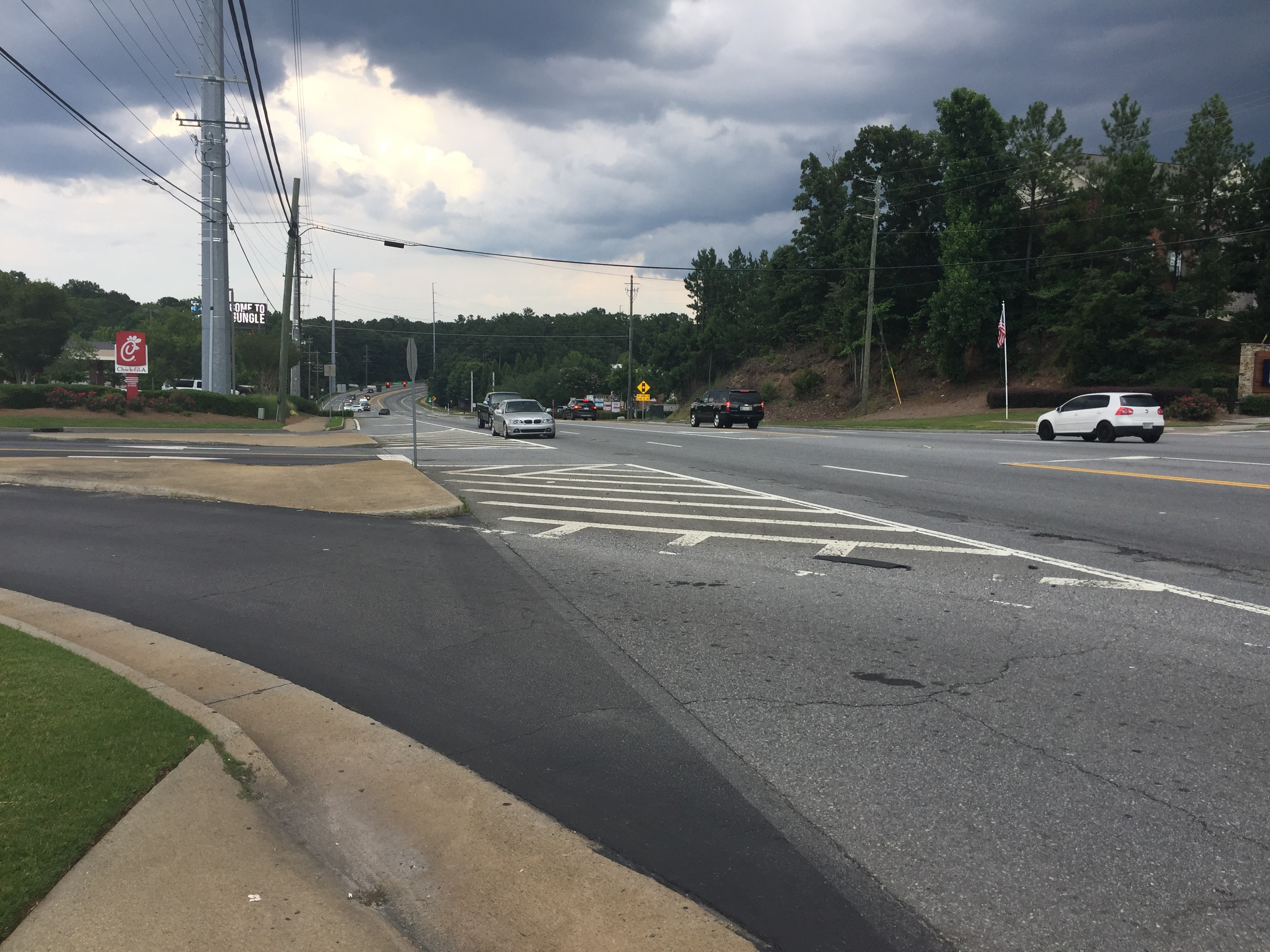 Multi-lane suburban road intersection with traffic signals, vehicles, and utility poles.