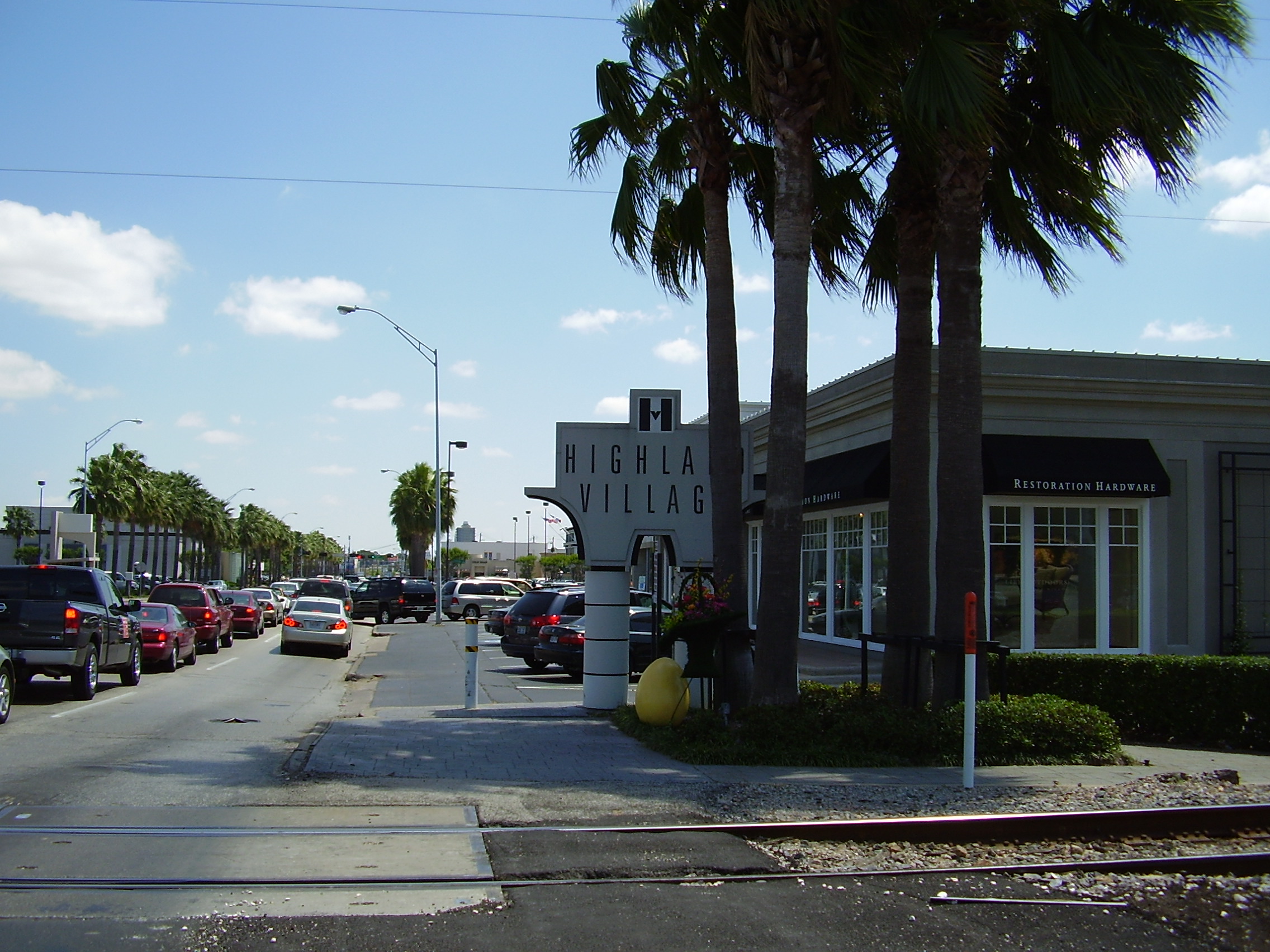Street-level view of a Highland Village shopping center entrance sign and storefronts.