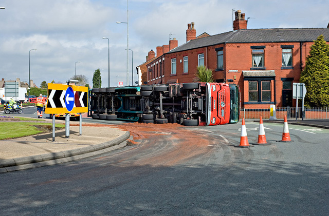 Large truck overturned on its side at an intersection, surrounded by traffic cones.