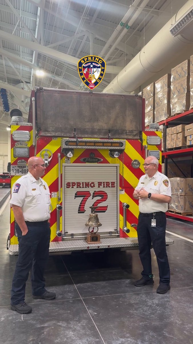 Two uniformed fire officials in white command shirts stand beside a red fire apparatus labeled Spring Fire 72.