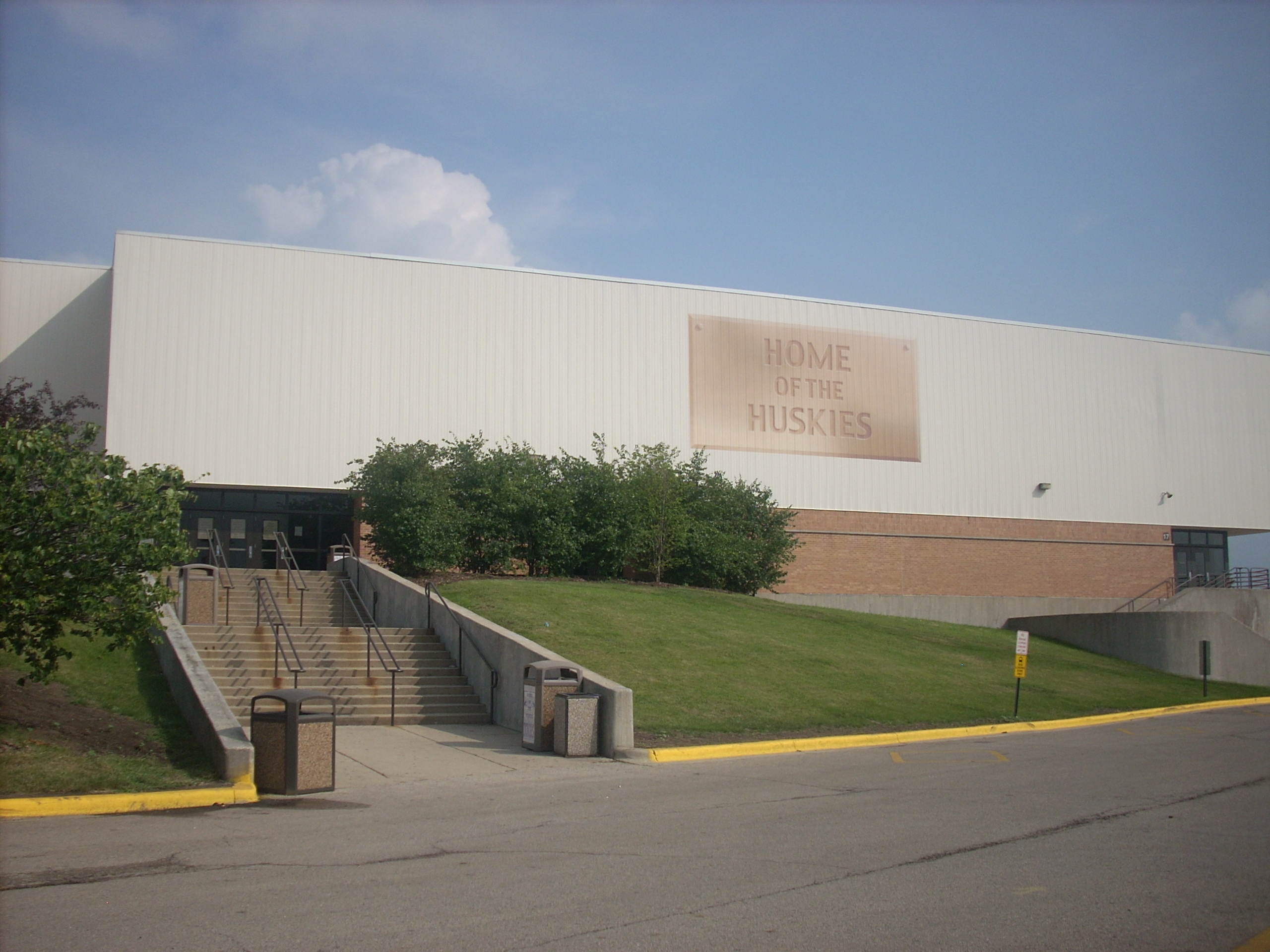 Exterior of a school athletic building with a 'Home of the Huskies' sign on a white metal facade.