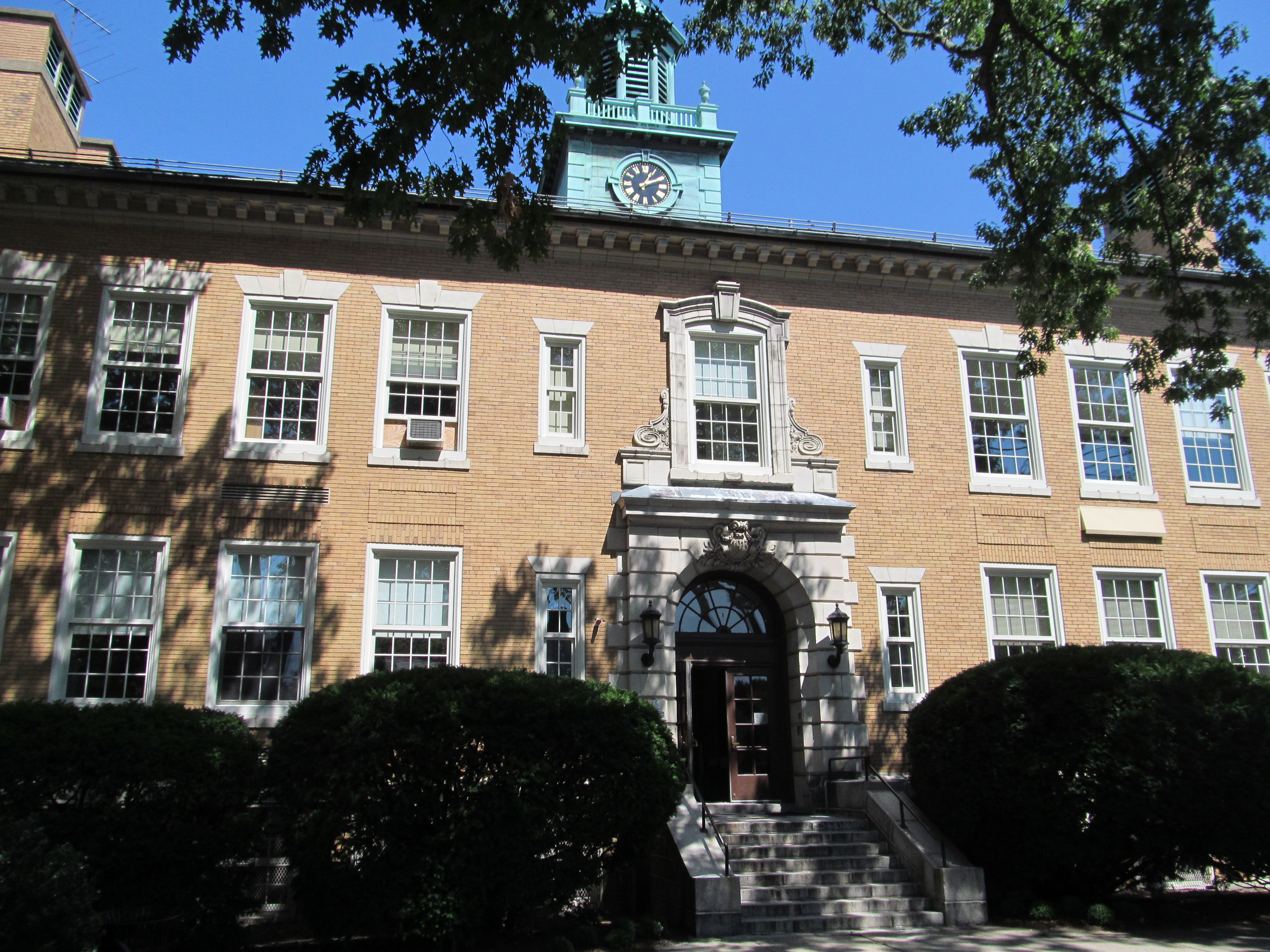 Multi-story brick school building with clock tower and stone entrance steps.