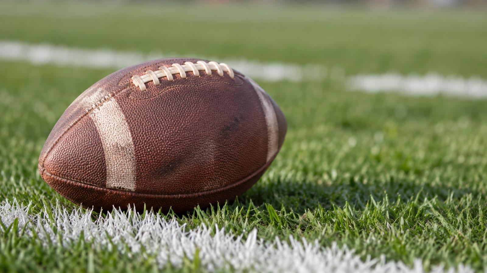 An American football resting on green grass beside a white yard line.