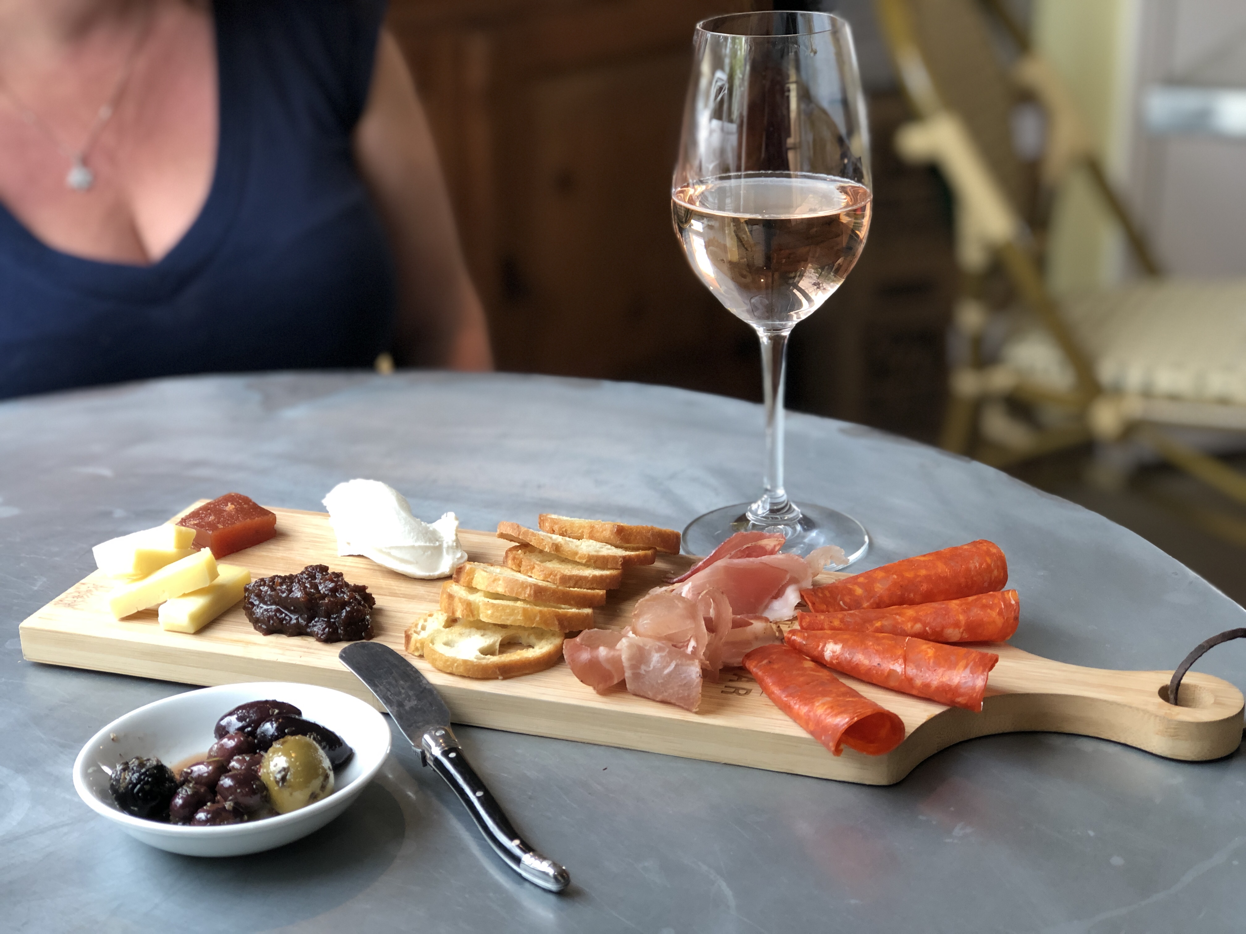 A glass of rosé wine beside a wooden charcuterie board with meats, cheese, and bread.