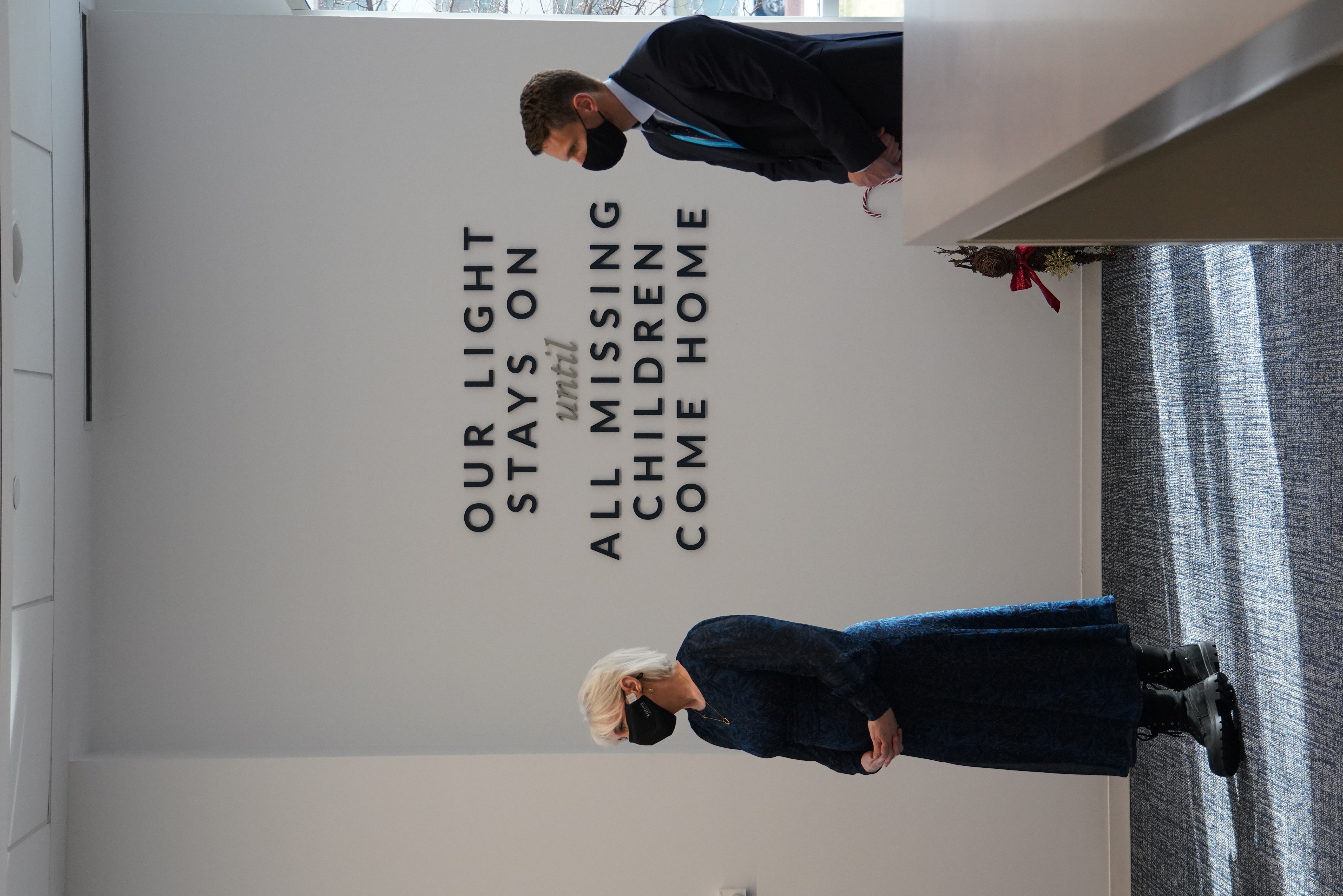 Two masked visitors stand in a lobby bearing a quote about missing children.