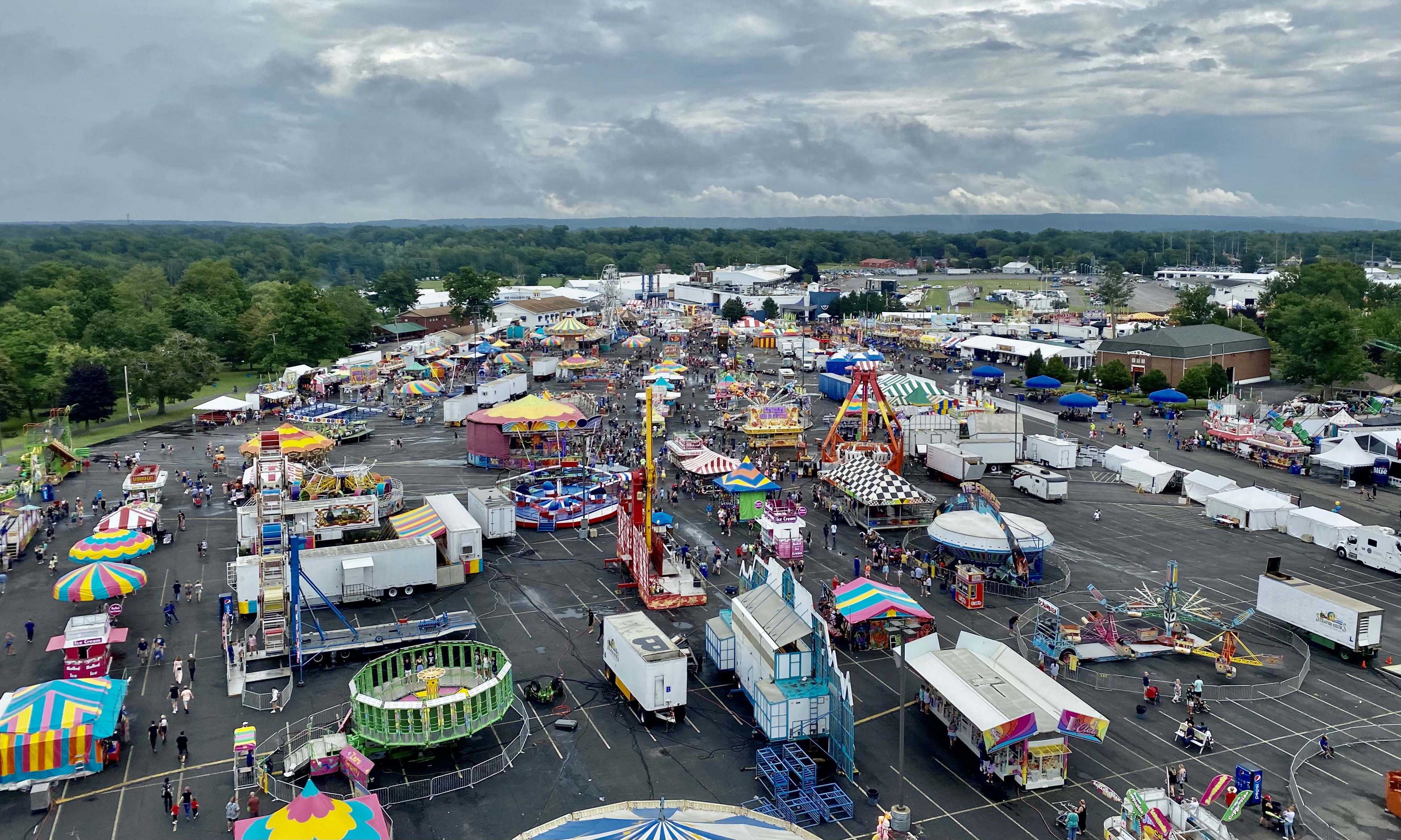 Aerial view of a county fair midway with carnival rides, tents, and crowds below.