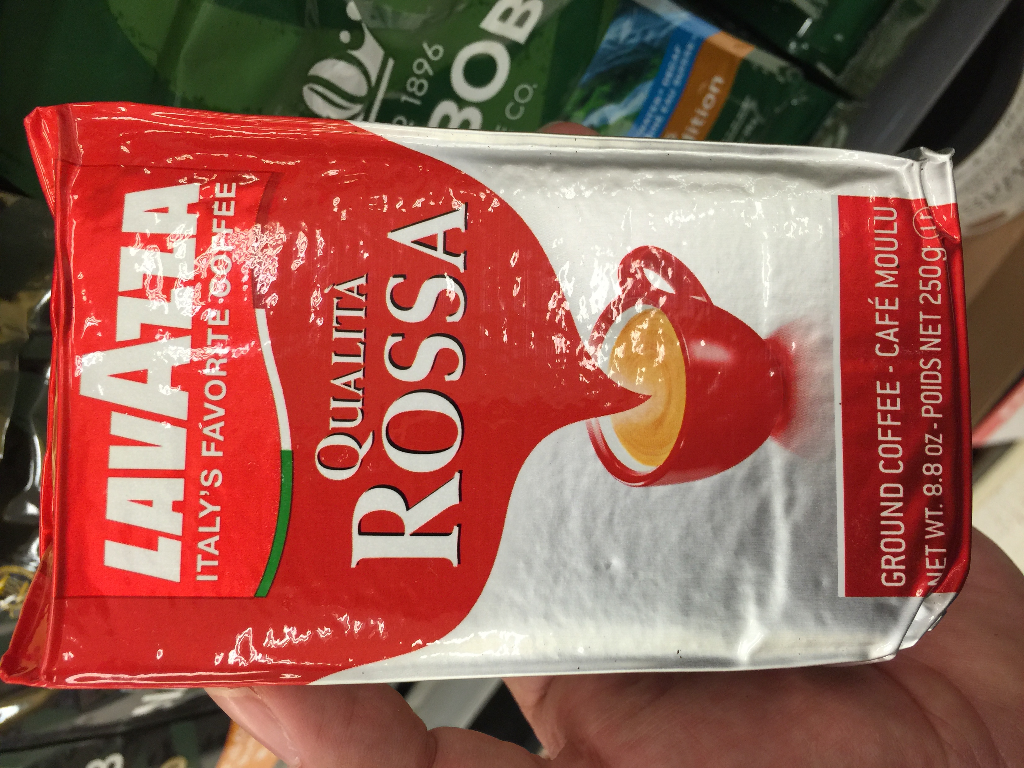 Hand holding a red and silver bag of Lavazza ground coffee.