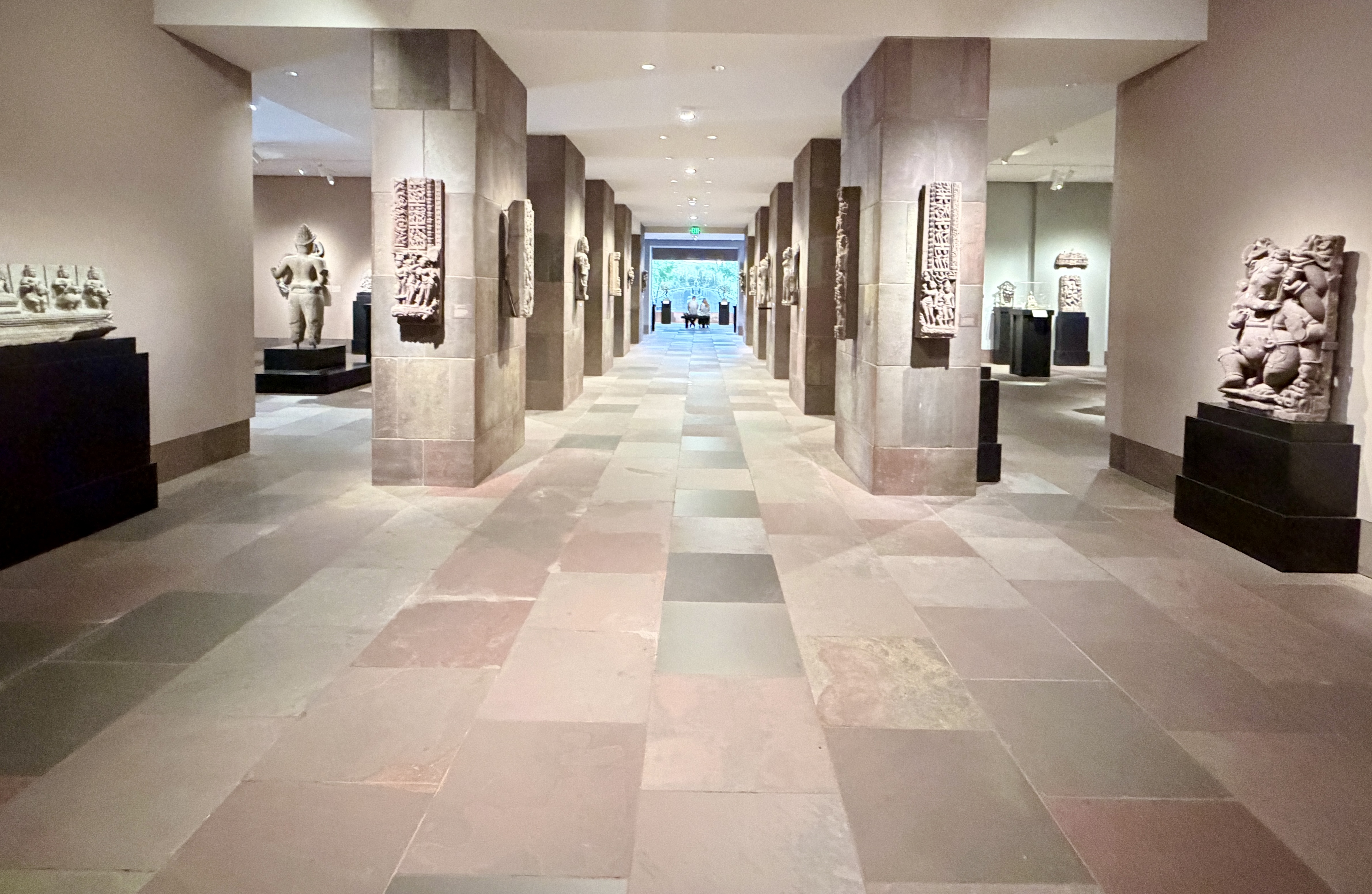 Long museum gallery corridor with stone columns and sculptures on pedestals.
