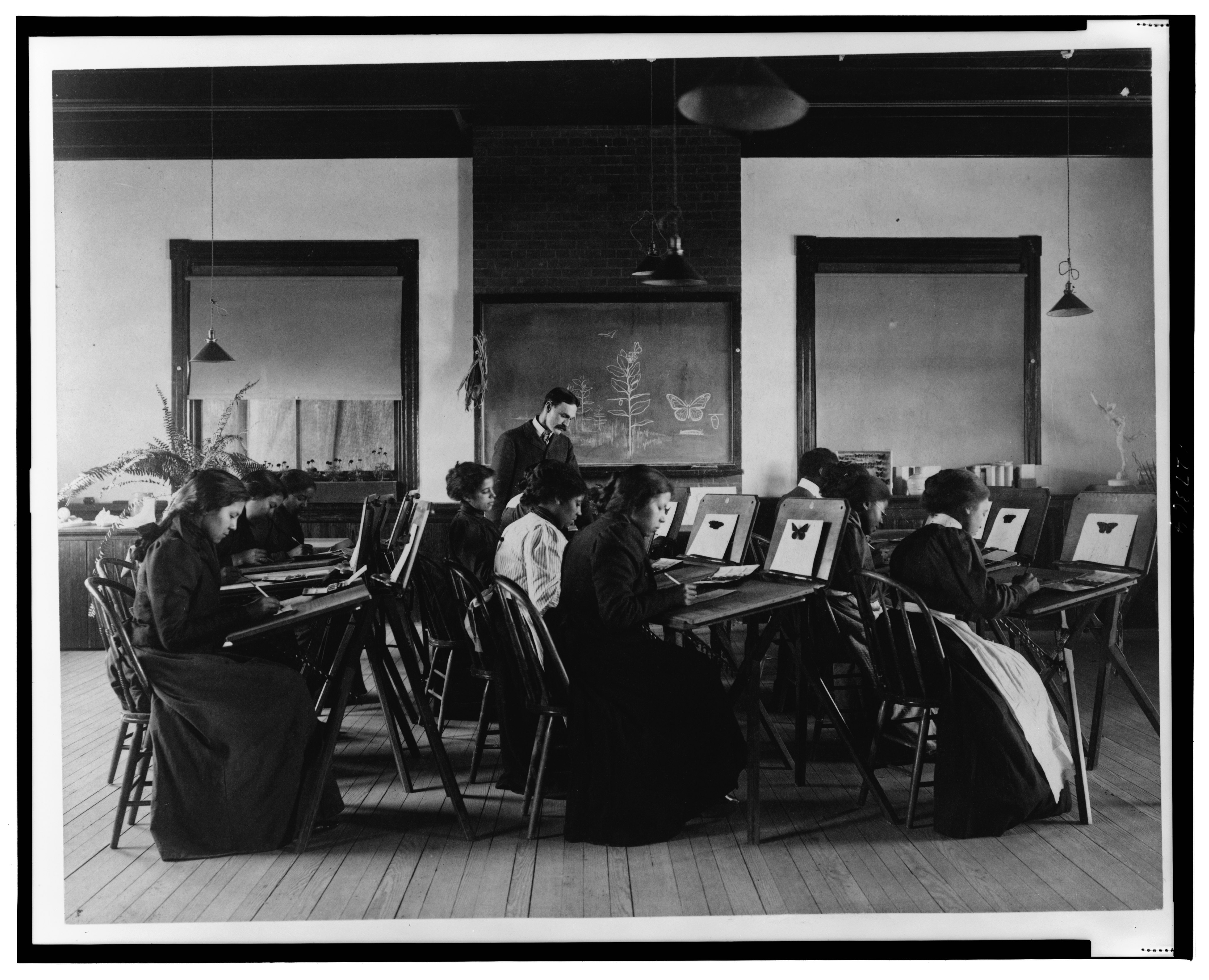A teacher stands at the front of a classroom as students work on watercolor paintings.