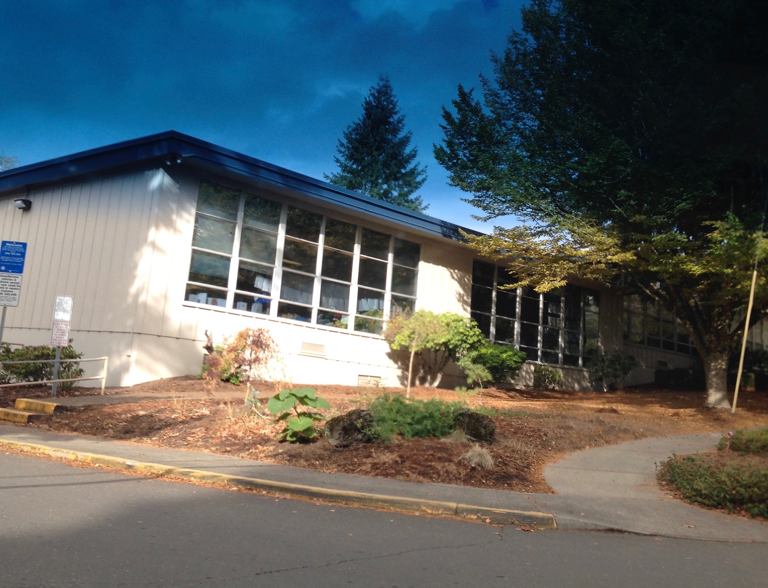Single-story school building with blue trim and large windows surrounded by trees.