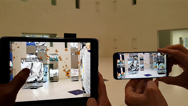 Two people hold a tablet and smartphone showing augmented reality overlays in a gallery.
