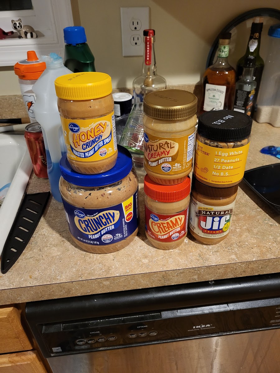 six jars of peanut butter all laid out on a counter.