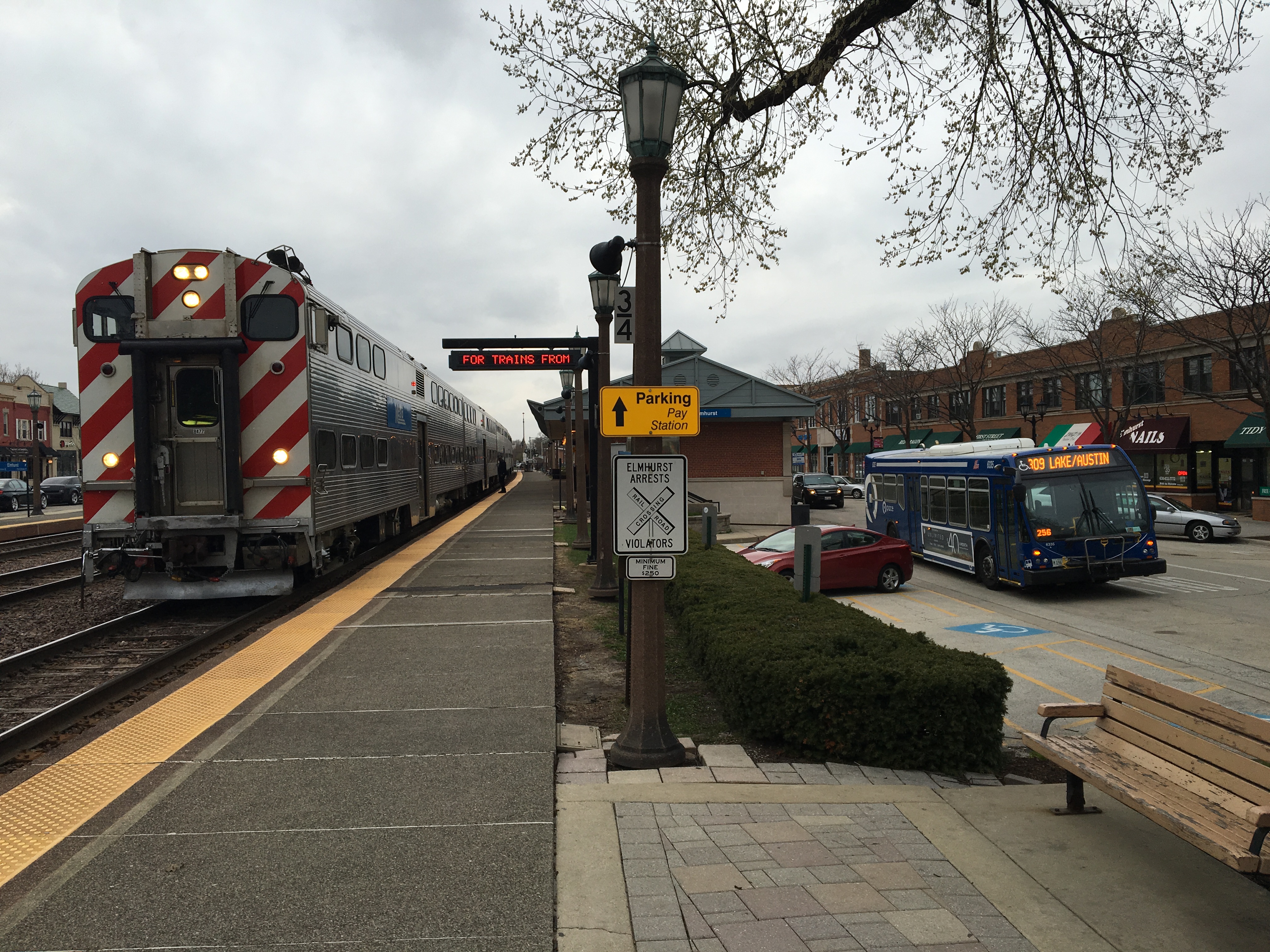 Metra commuter train stopped at a suburban station platform with a Pace bus nearby.