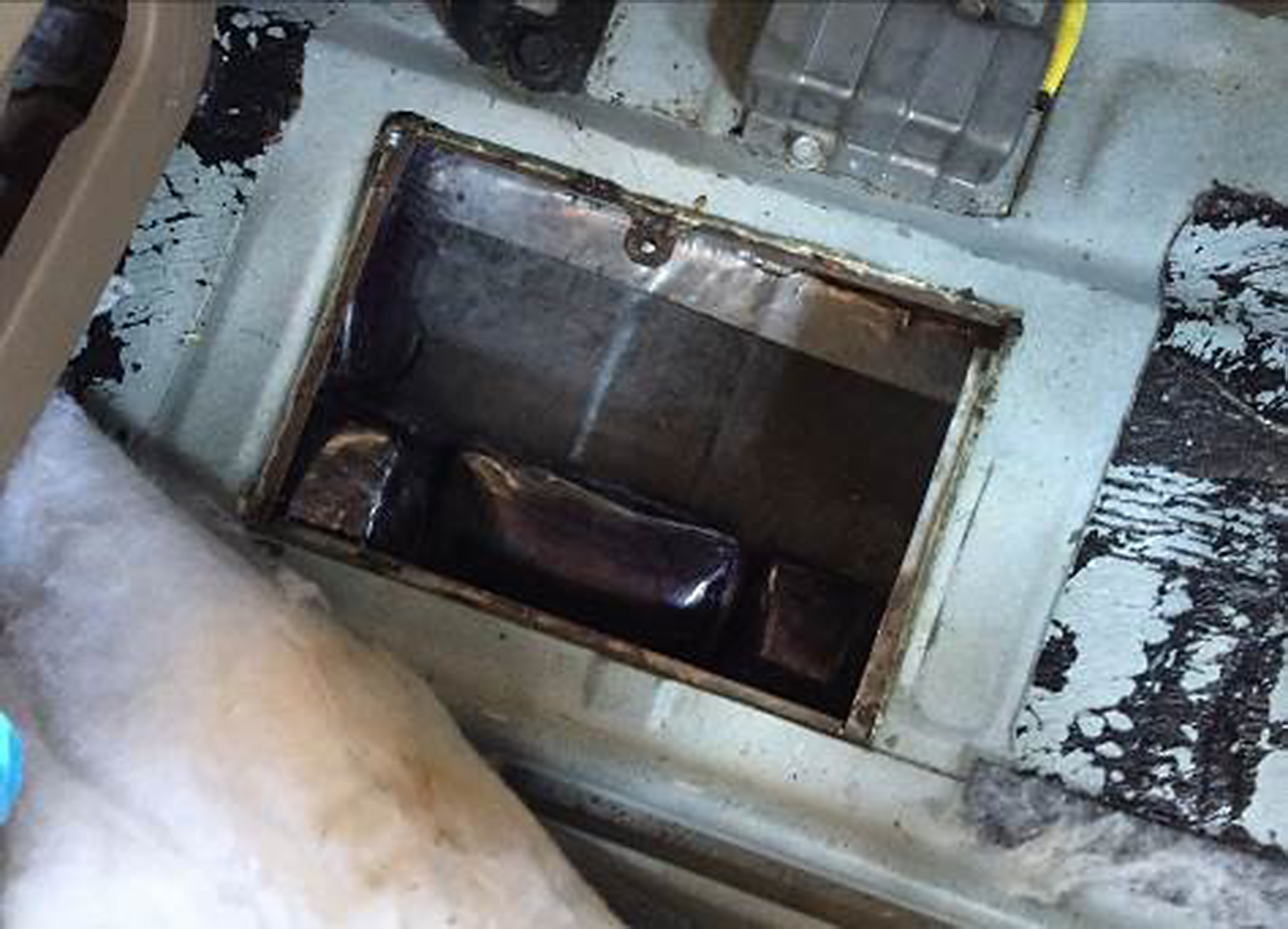 Dark packages visible inside an open, rusted vehicle tank compartment.