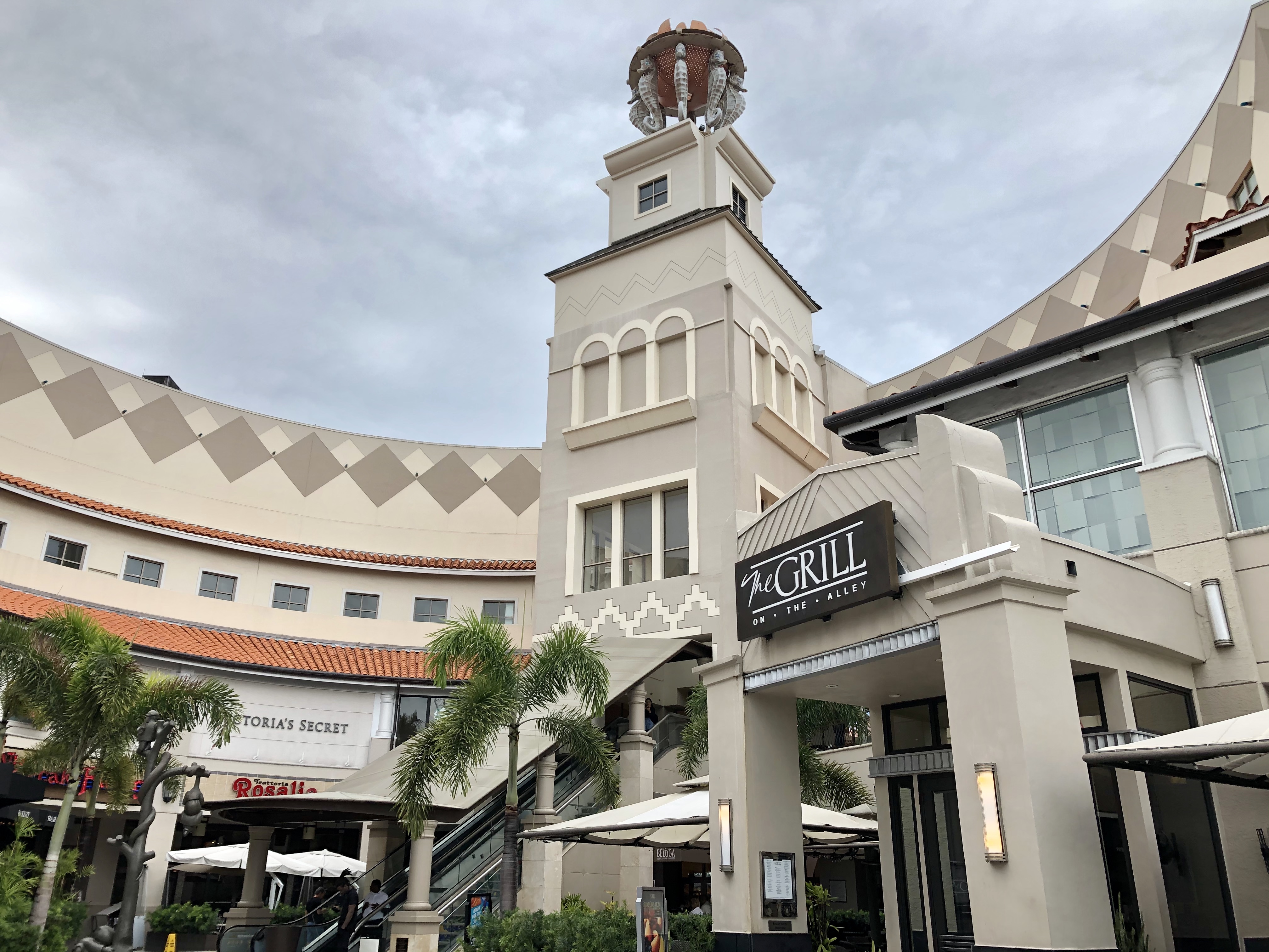Shopping mall exterior with a clock tower, palm trees, and retail storefronts.