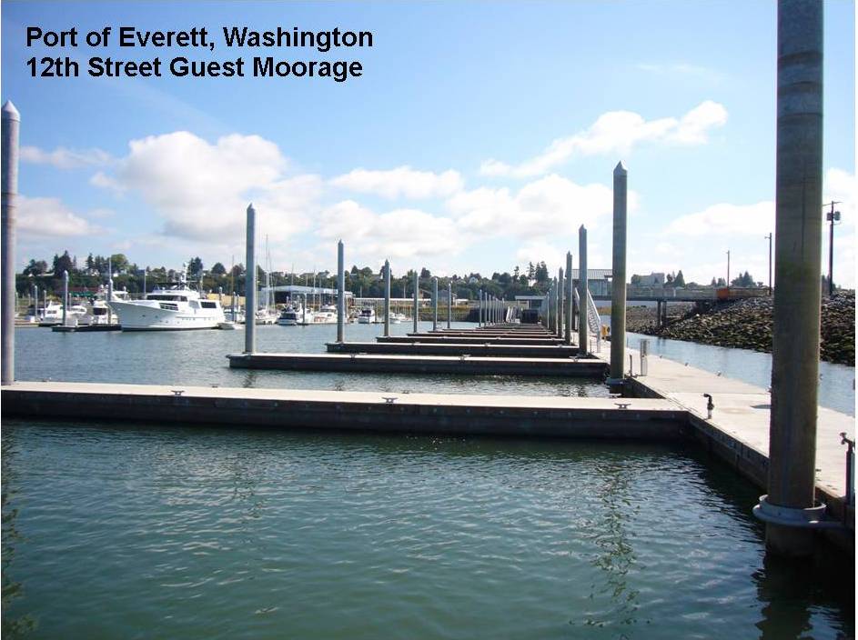 Concrete floating dock with tall wooden pilings and boats moored behind it.