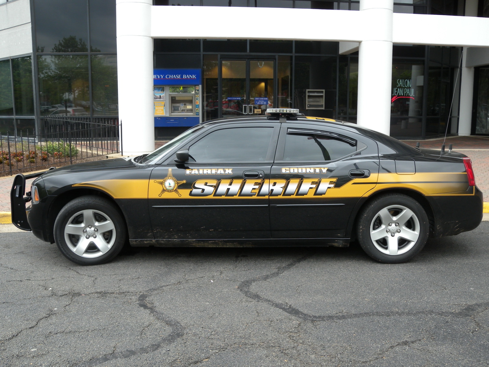 A black and gold Fairfax County Sheriff's Office Dodge Charger patrol car parked outside.
