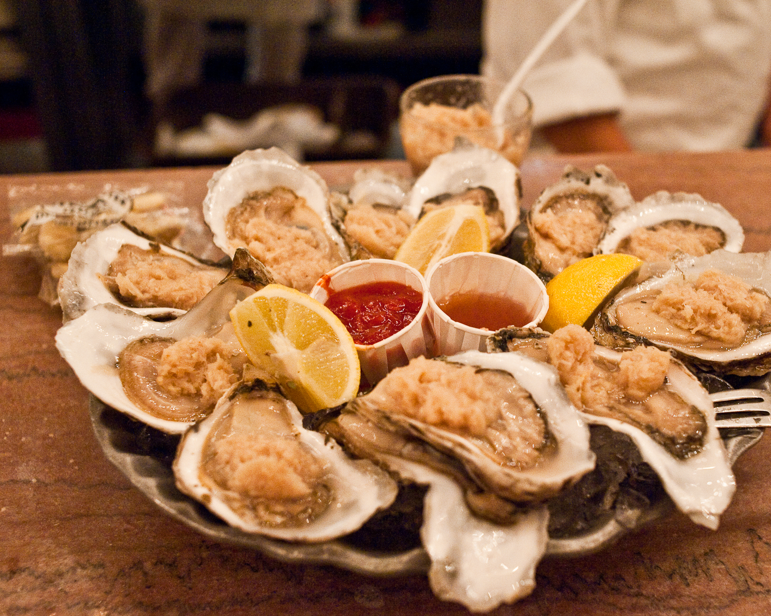 Platter of raw oysters on the half shell with lemon wedges and cocktail sauce.
