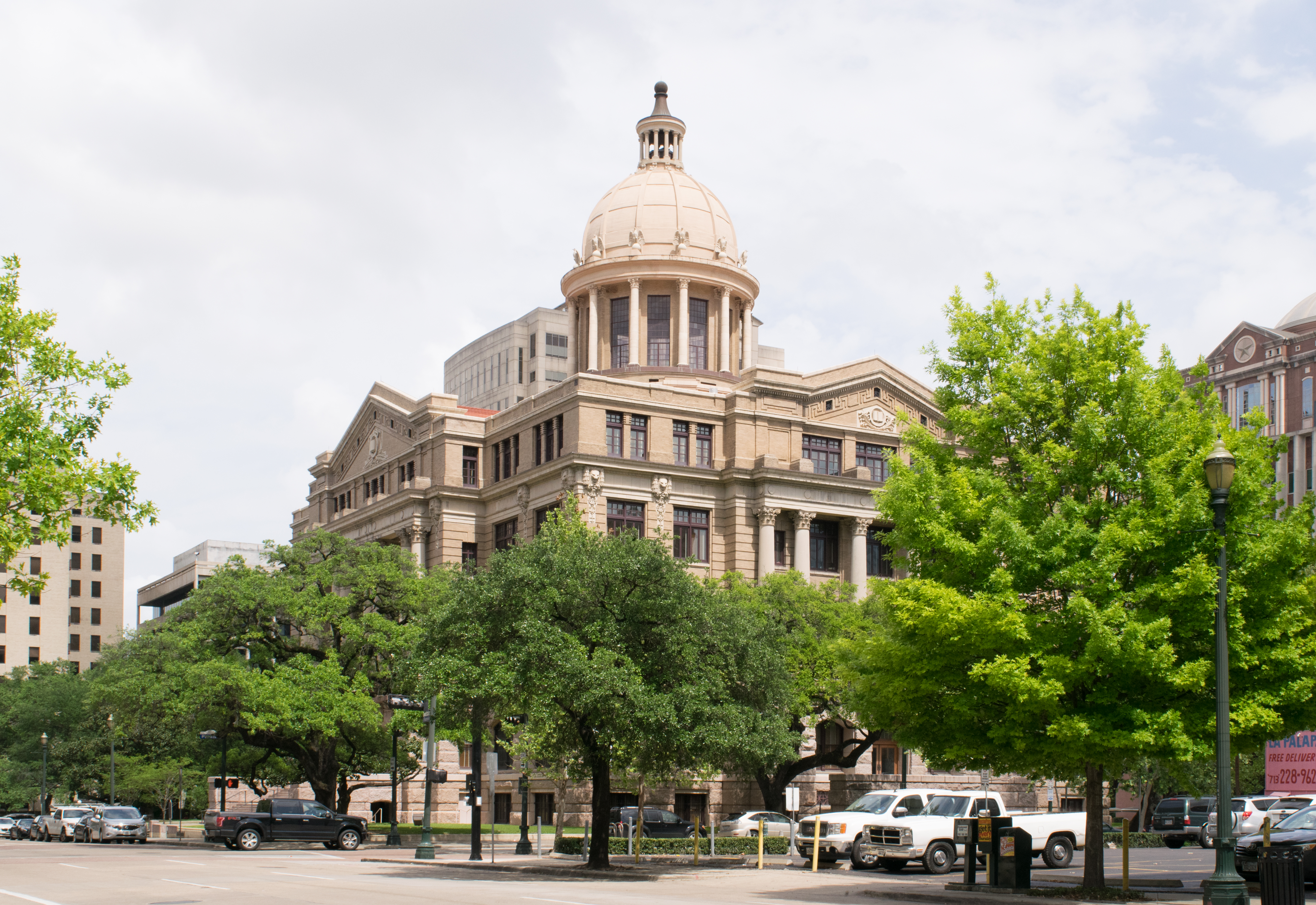 Domed neoclassical courthouse building at a street corner, framed by mature trees.
