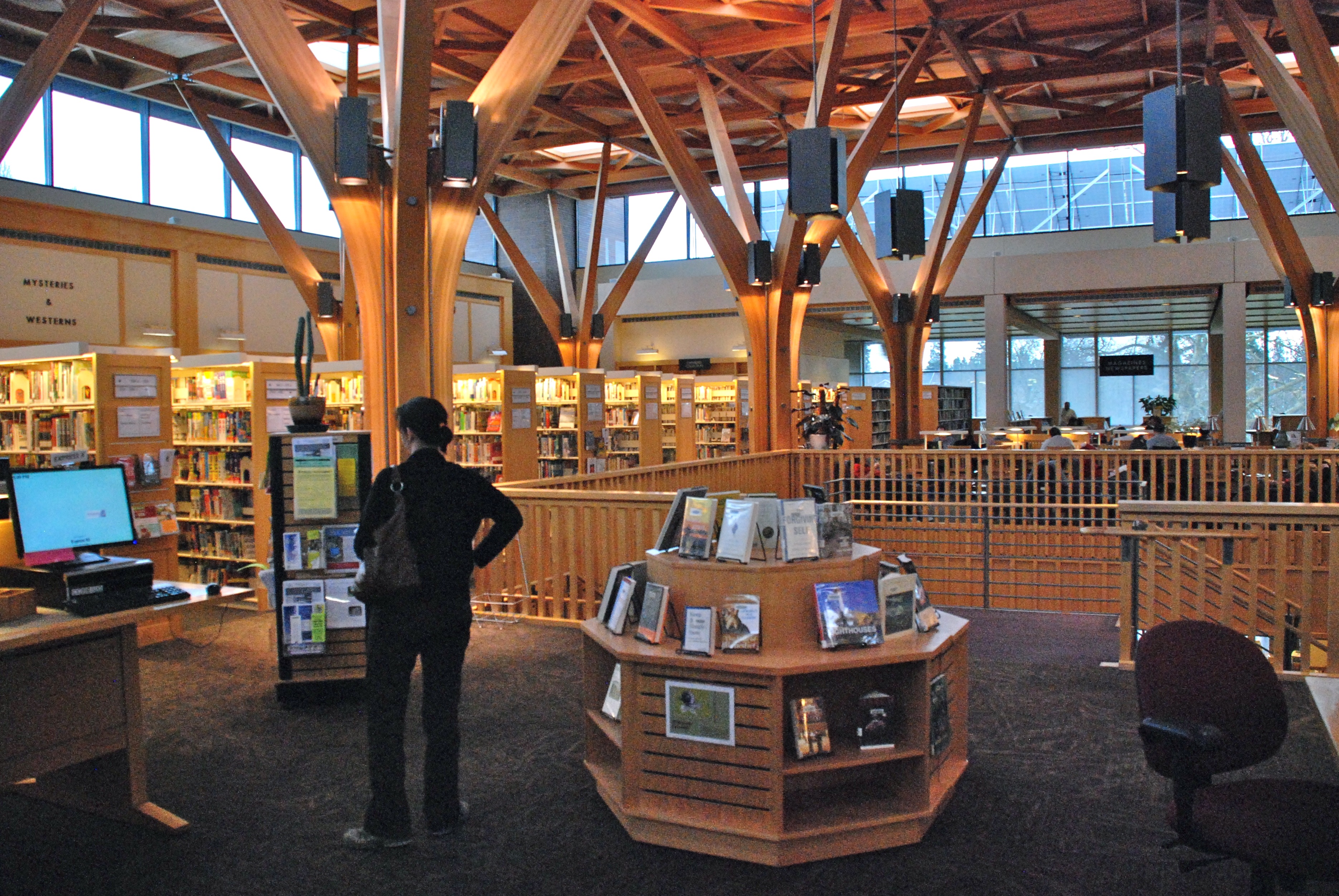 Library interior with distinctive wooden beams, bookshelves lining the walls, and a central display kiosk.