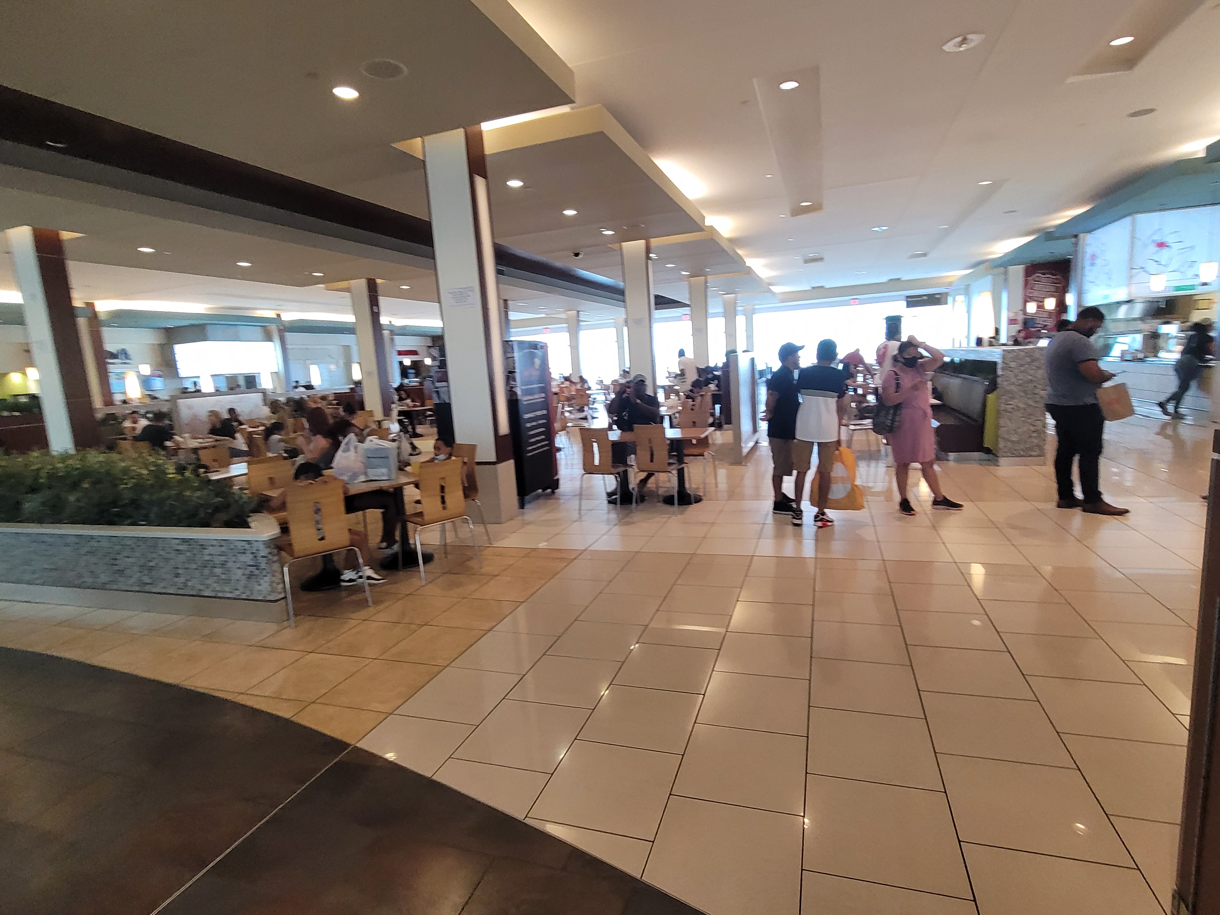 People seated and walking inside a large indoor shopping mall common area.