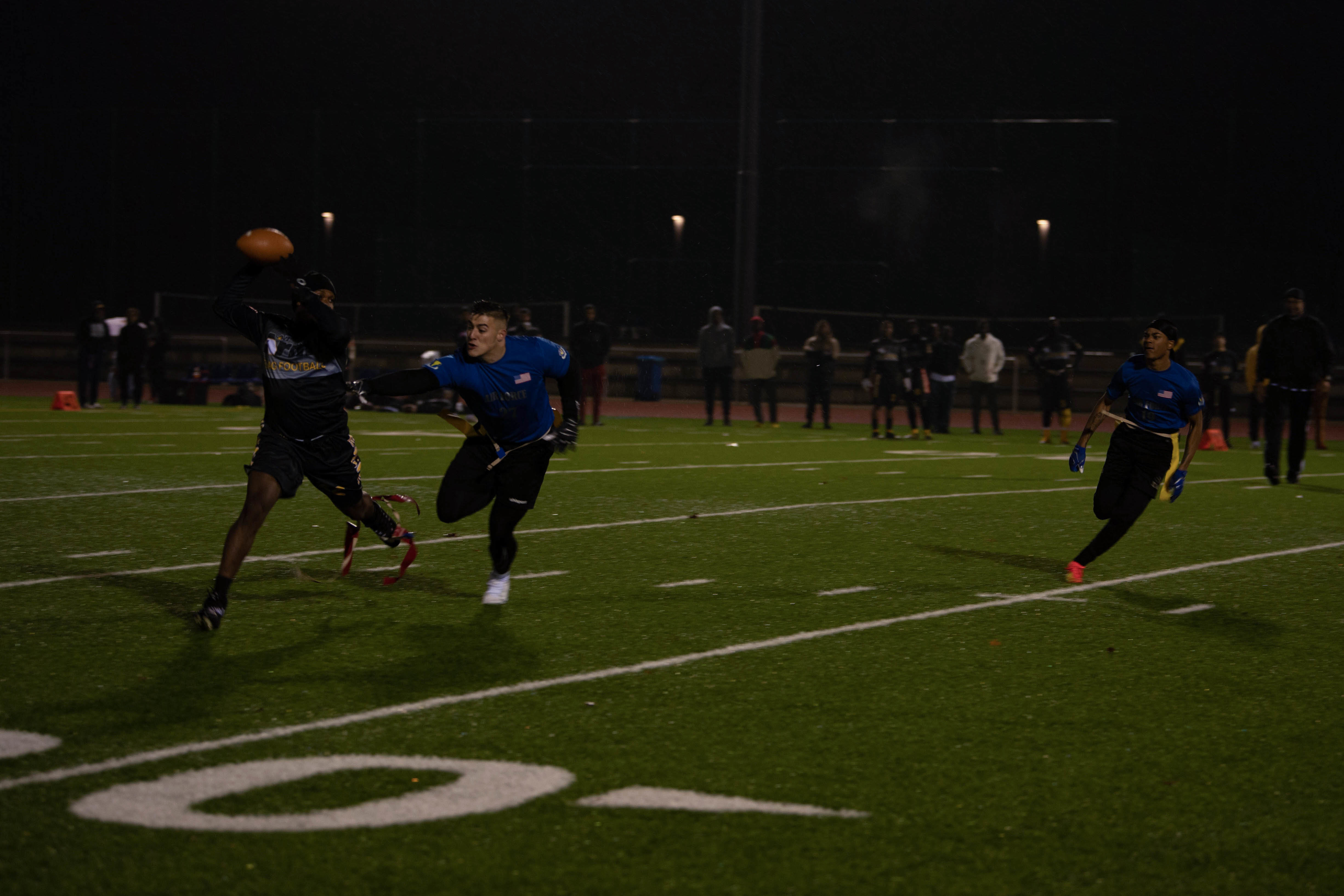 Three players compete in a flag football game on a lit field at night.