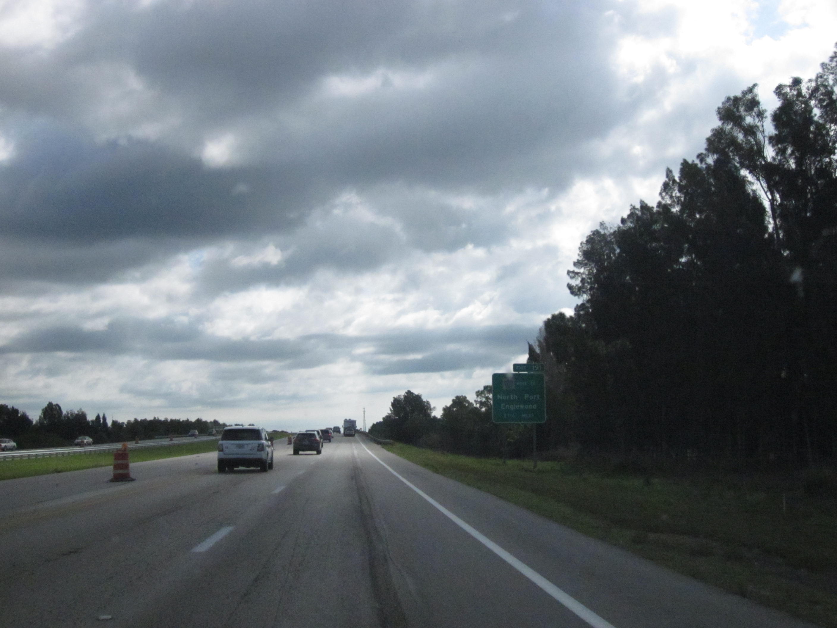Vehicles on a multi-lane divided interstate highway with green signs and tree lines on both sides.