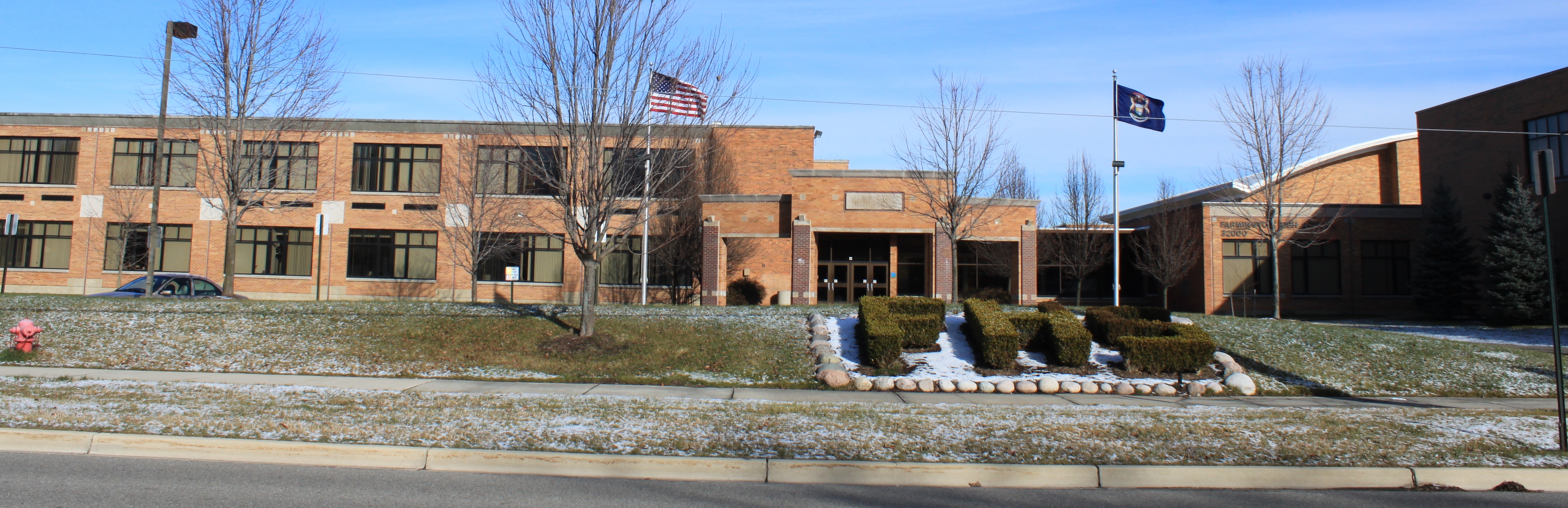 Two-story brick high school building with flagpoles and snow-dusted lawn.
