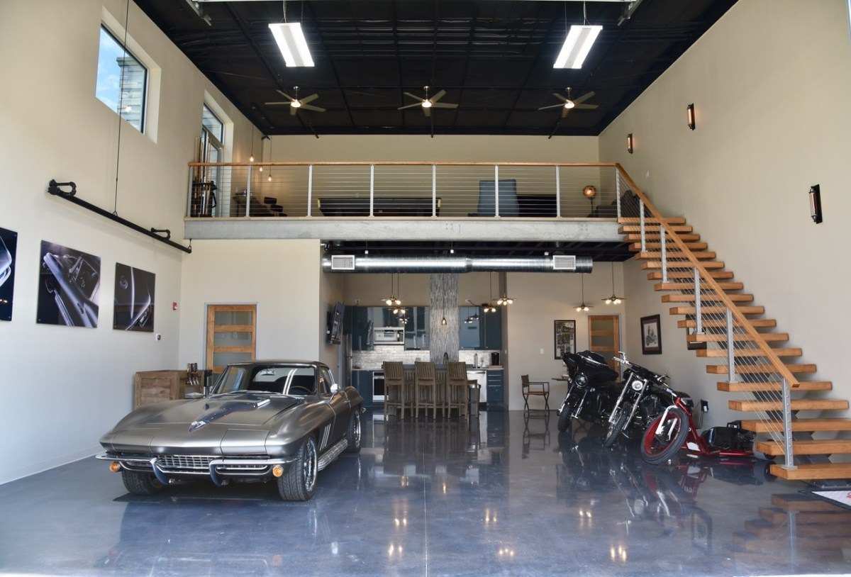 Luxury garage interior with a classic Corvette, motorcycles, mezzanine level, and polished concrete floors.