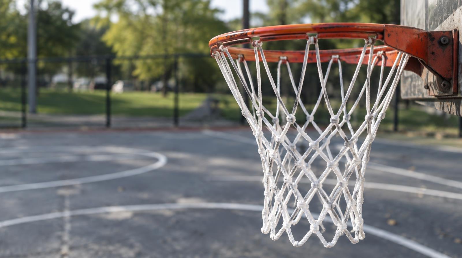 New white nylon basketball net hanging from an outdoor metal rim over asphalt.