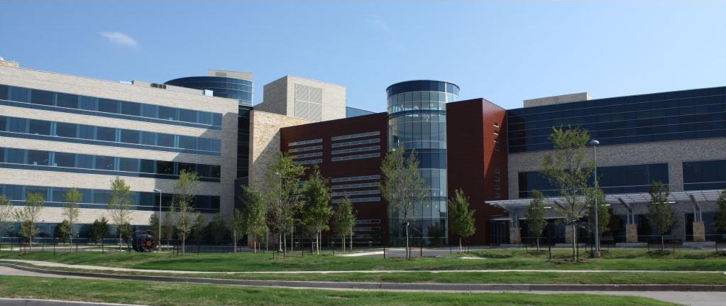 Multi-story hospital complex with a cylindrical glass tower and red brick facade.