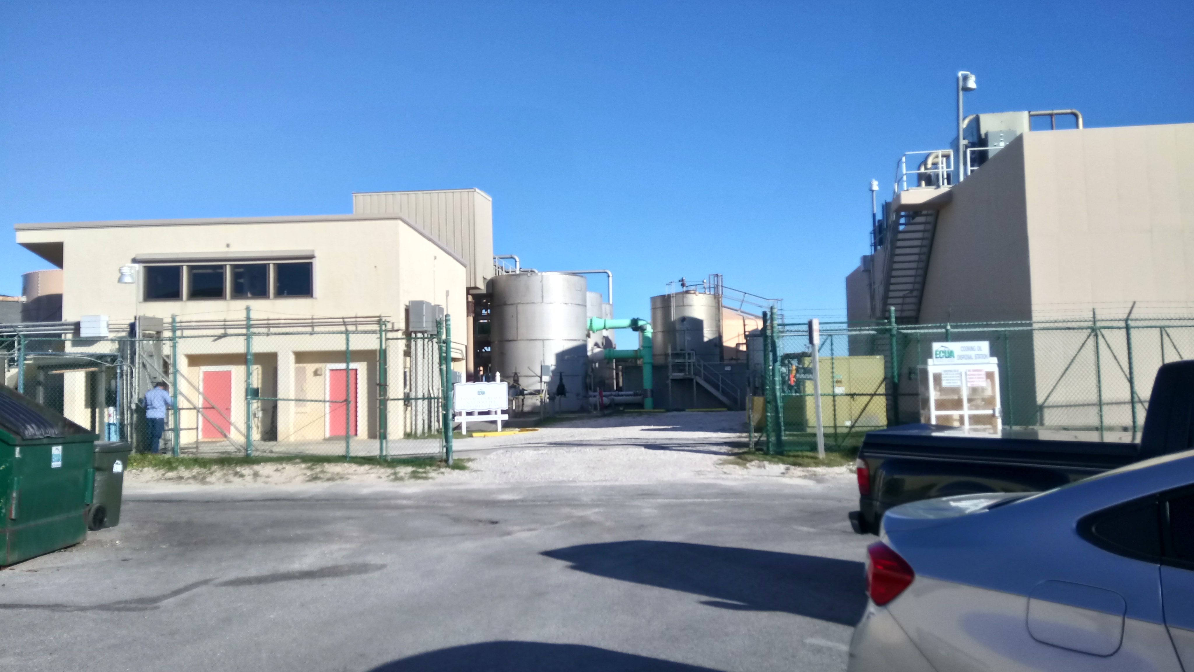 Exterior of a wastewater treatment plant with large cylindrical tanks and chain-link fencing.