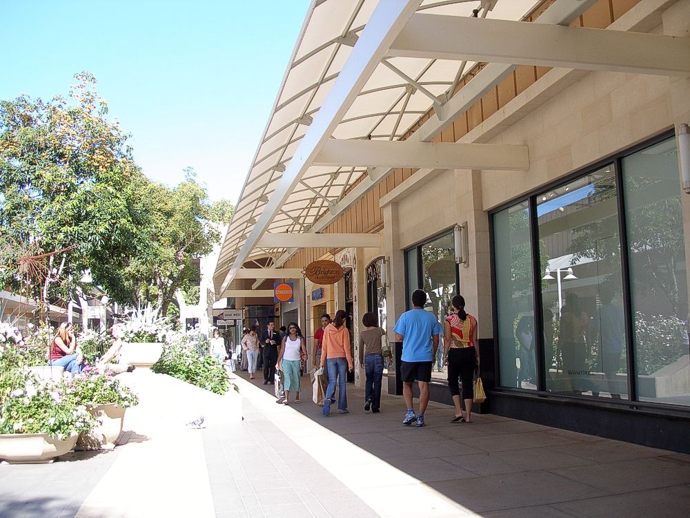 Shoppers walk along a covered outdoor corridor at an upscale shopping center.