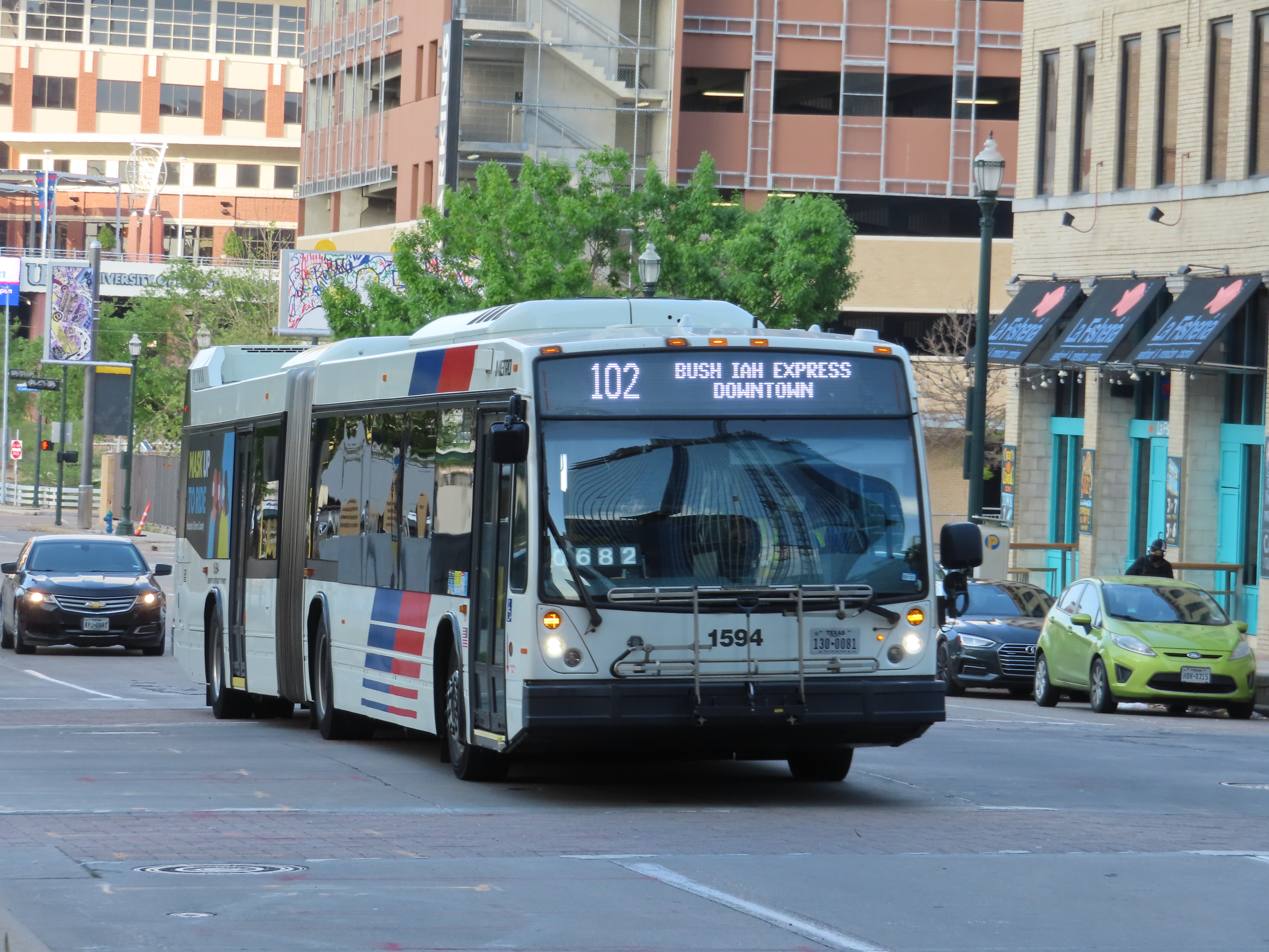 A large articulated METRO bus moves along a downtown Houston street.