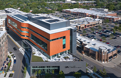 Aerial view of a modern multi-story building with orange cladding and rooftop solar panels.