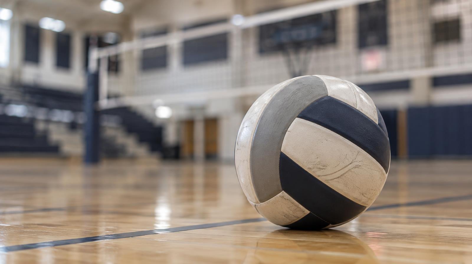 A volleyball resting on a hardwood gymnasium floor near the net.
