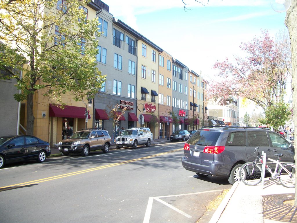 Downtown street with storefronts, parked cars, and a sidewalk bicycle rack.