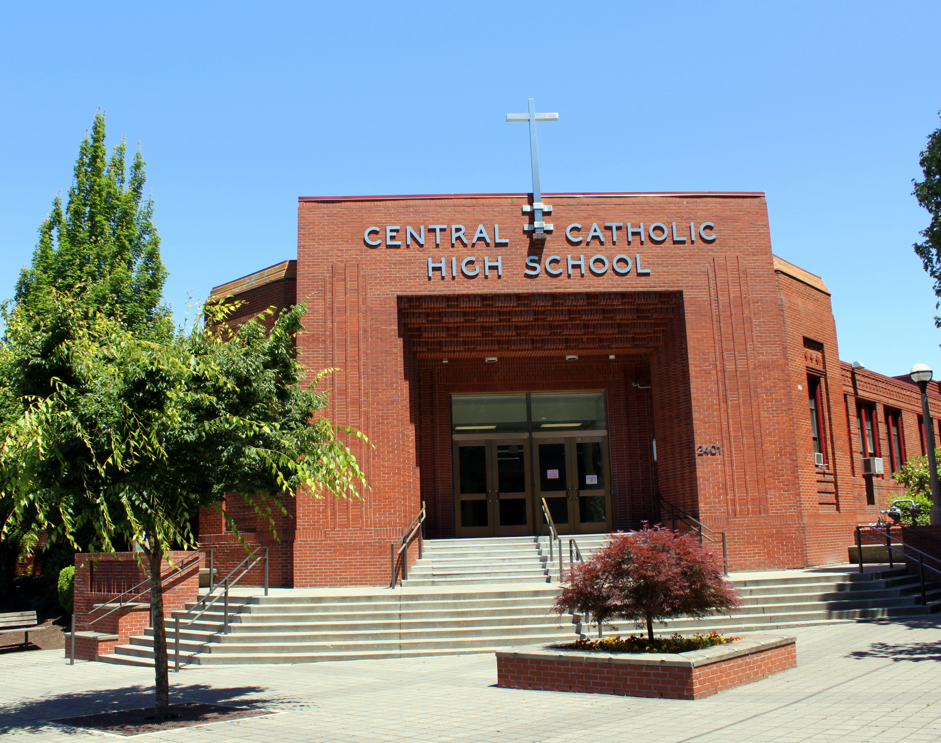 Red-brick school building with name in metal letters and a cross above the entrance.