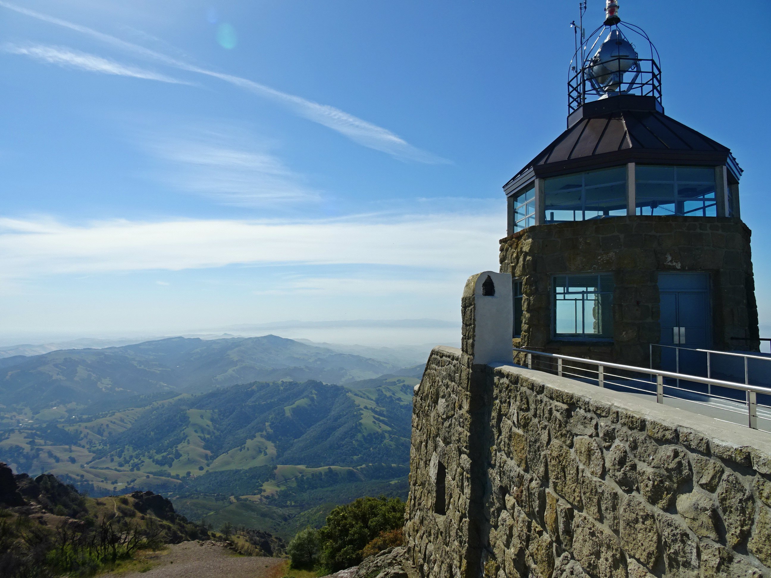 Stone observation building at a mountain summit with sweeping views of green hills.