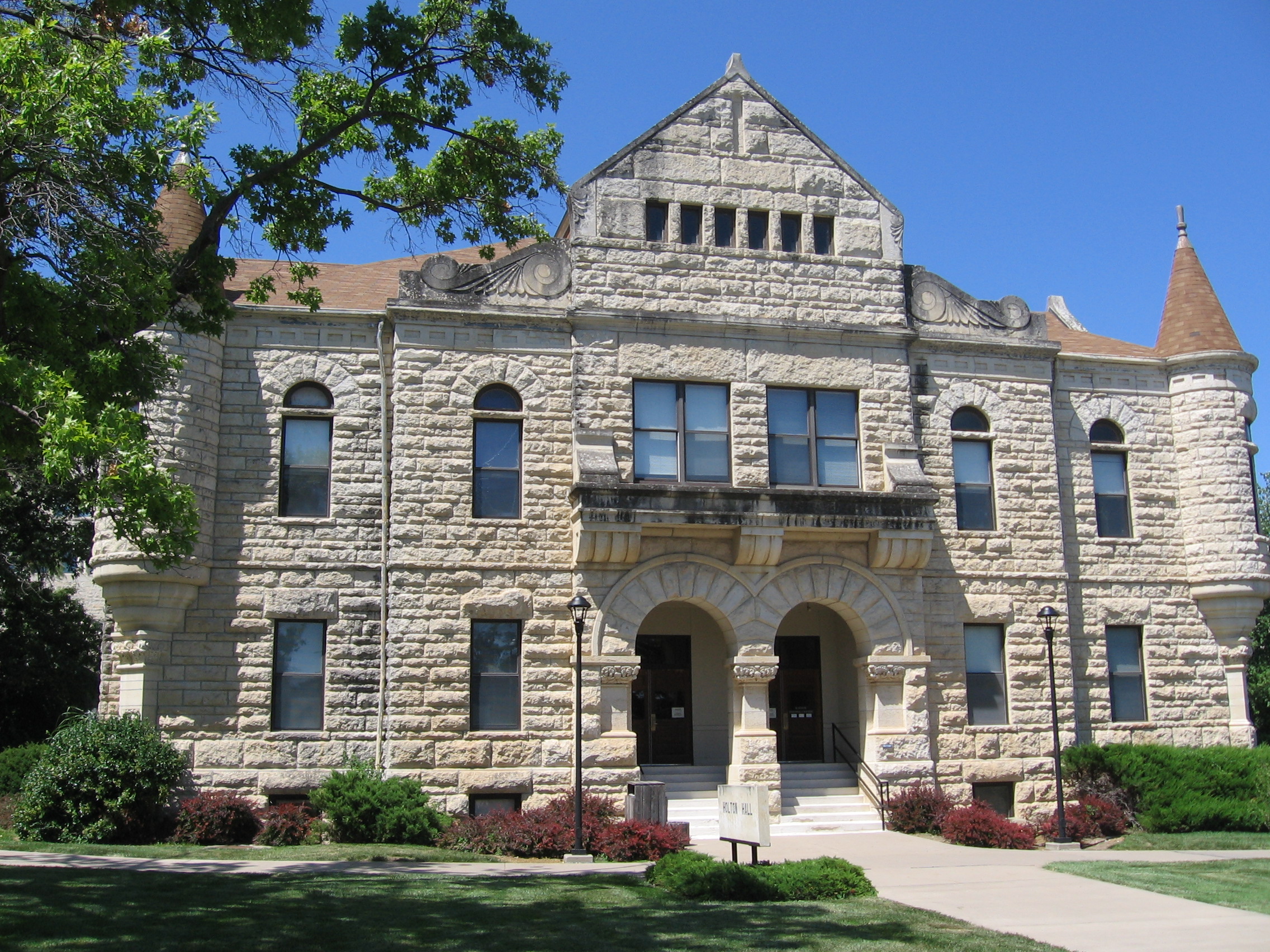 Limestone academic building with arched windows and corner turret on a university campus.