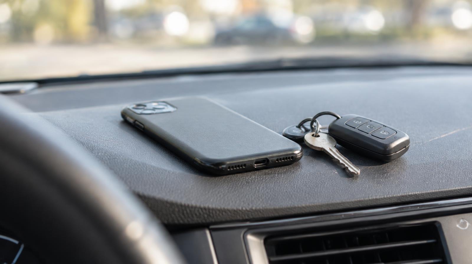 A face-down smartphone and car keys resting on a car dashboard.