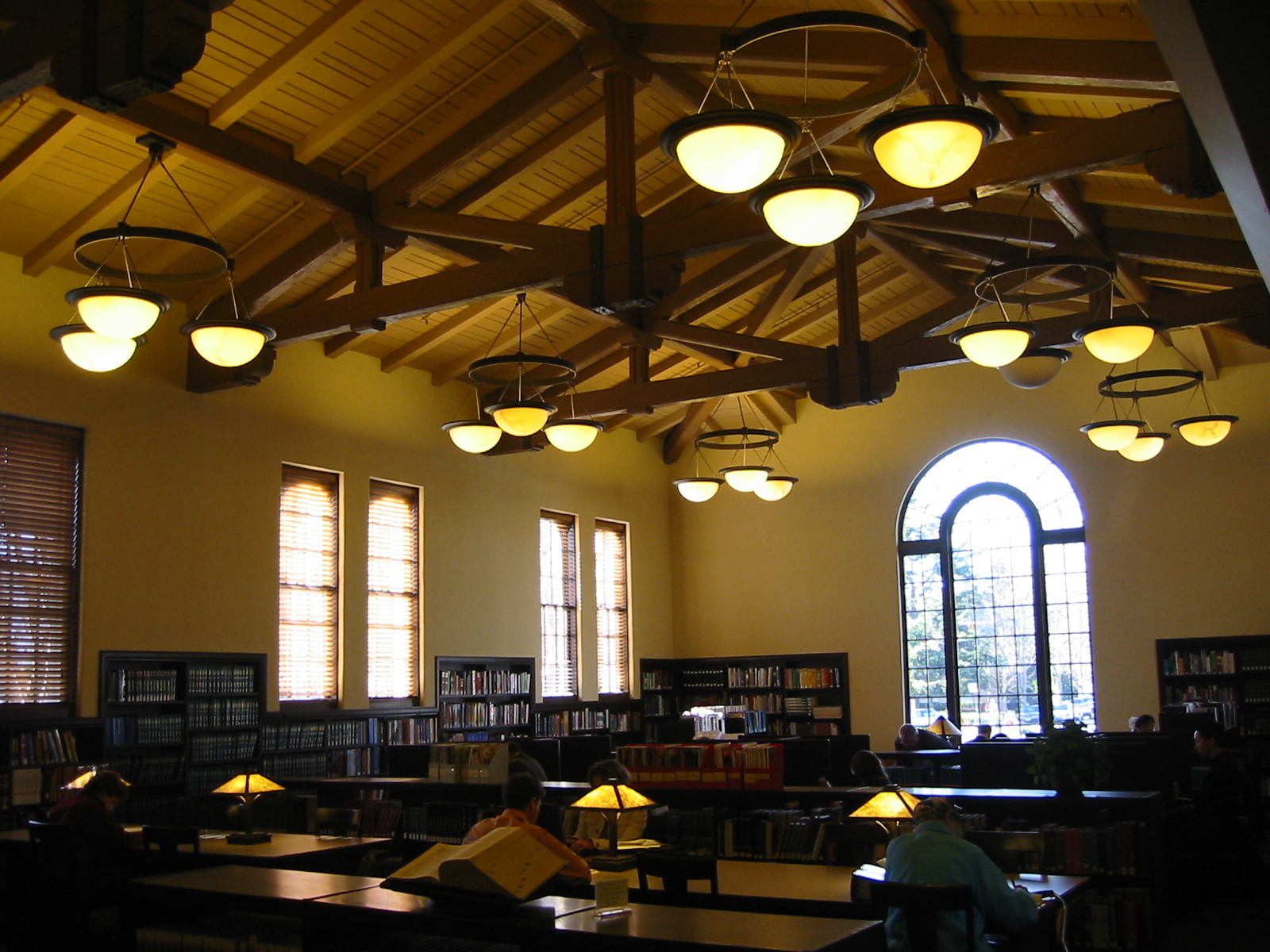 Library reading room with vaulted wooden ceiling, globe pendant lights, and bookshelves lining the walls.