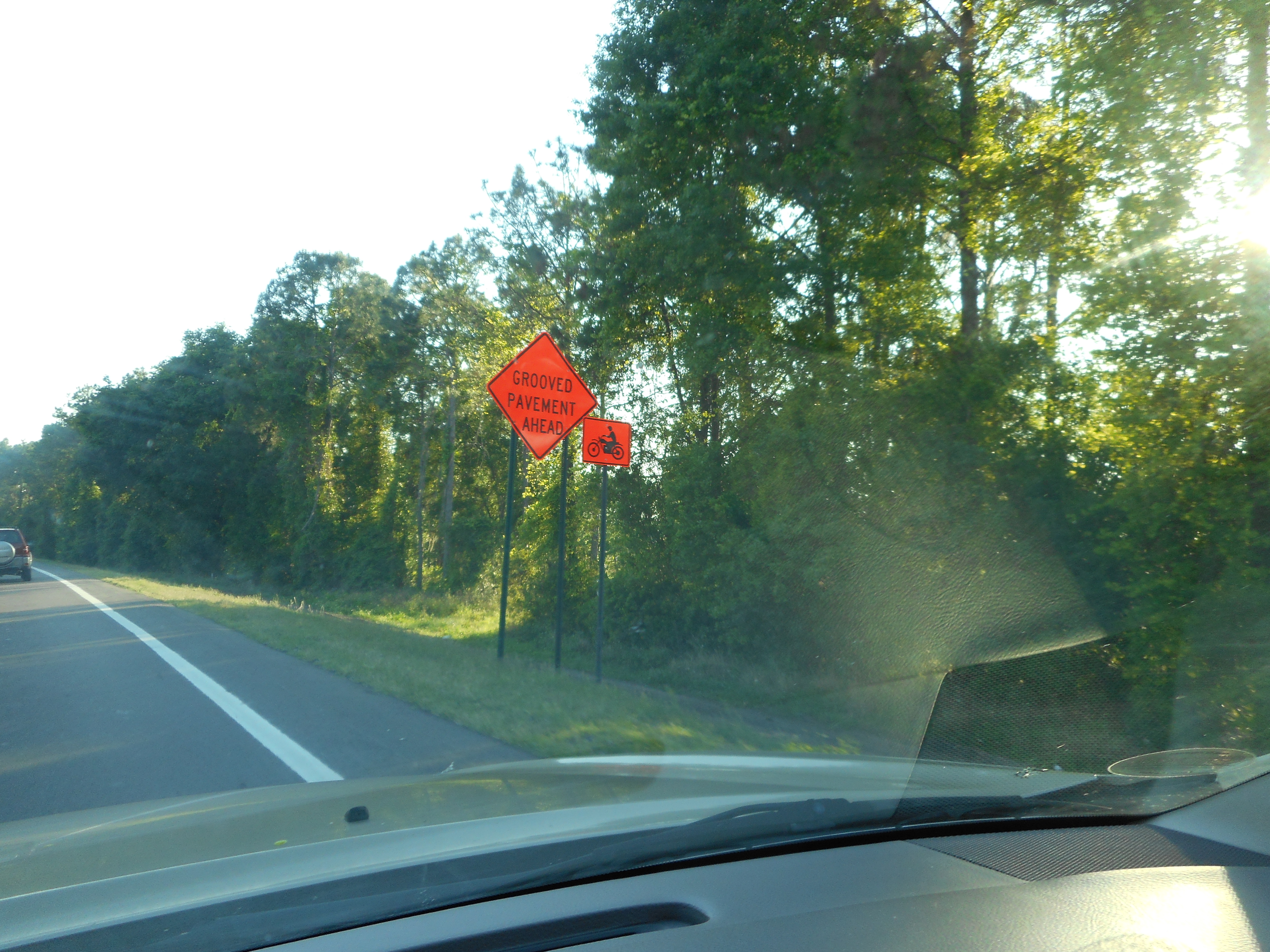 Orange construction warning sign posted along a tree-lined highway in Pasco County, Florida.