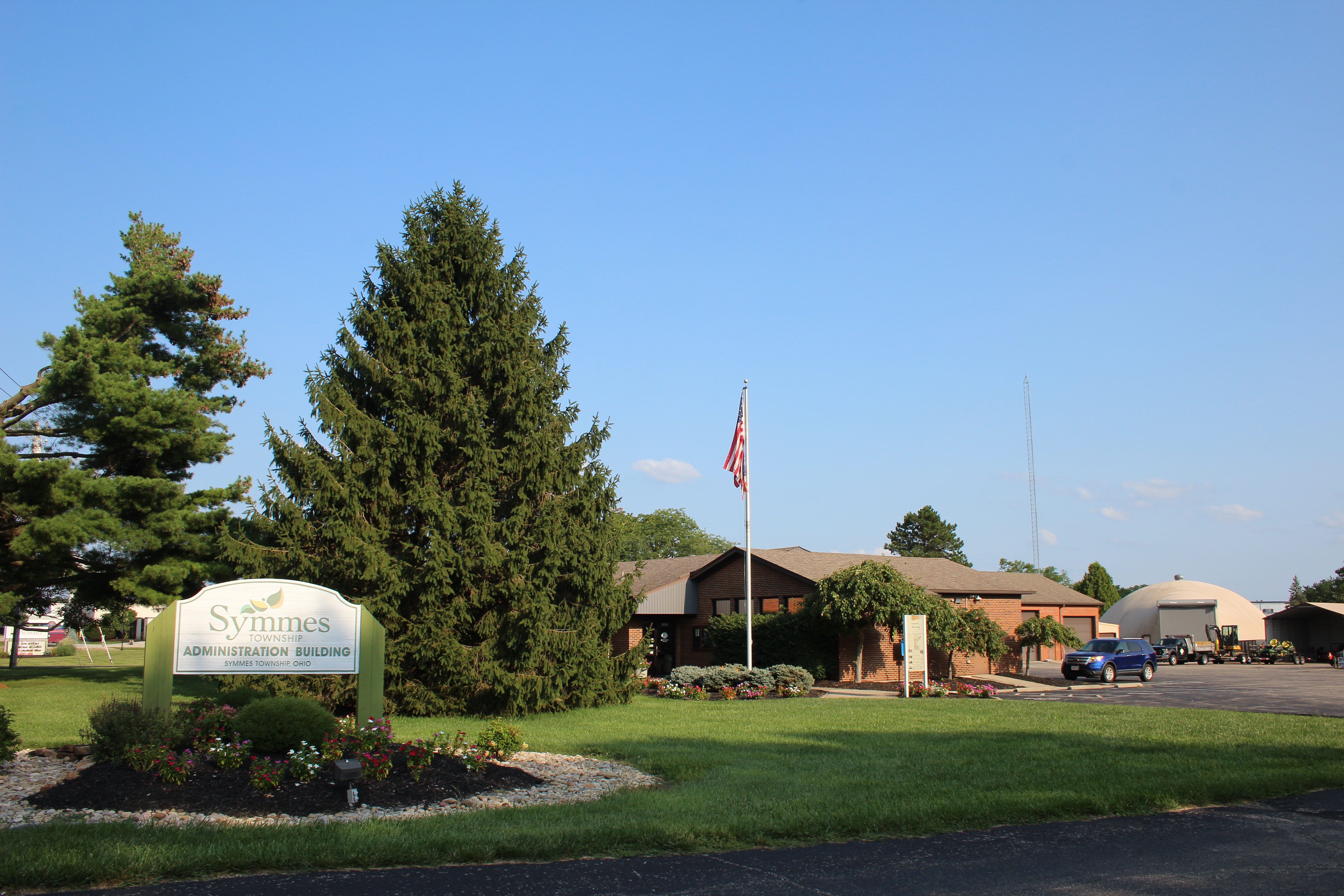 Single-story brick township administration building with a sign and American flag out front.