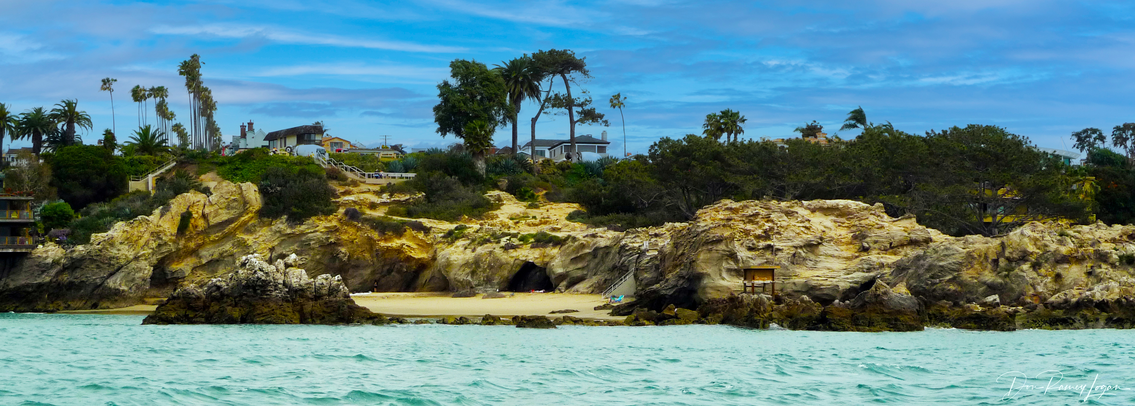 Rocky sandstone cliffs frame a small sandy cove with turquoise water below.