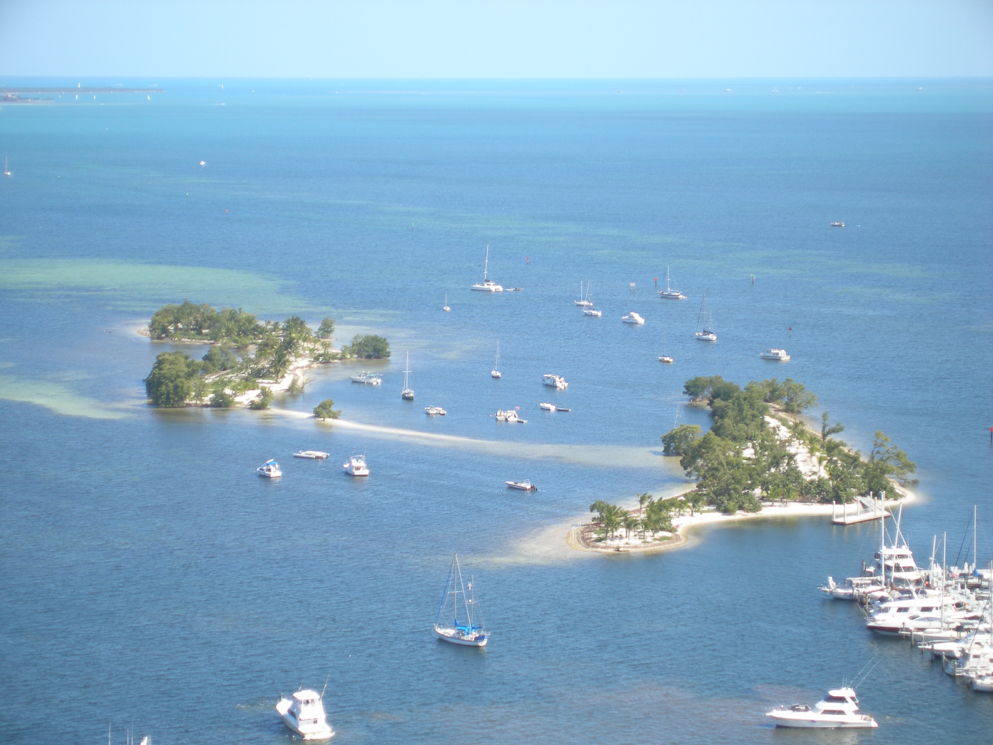Aerial view of Biscayne Bay with dozens of boats anchored in turquoise water near small islands.