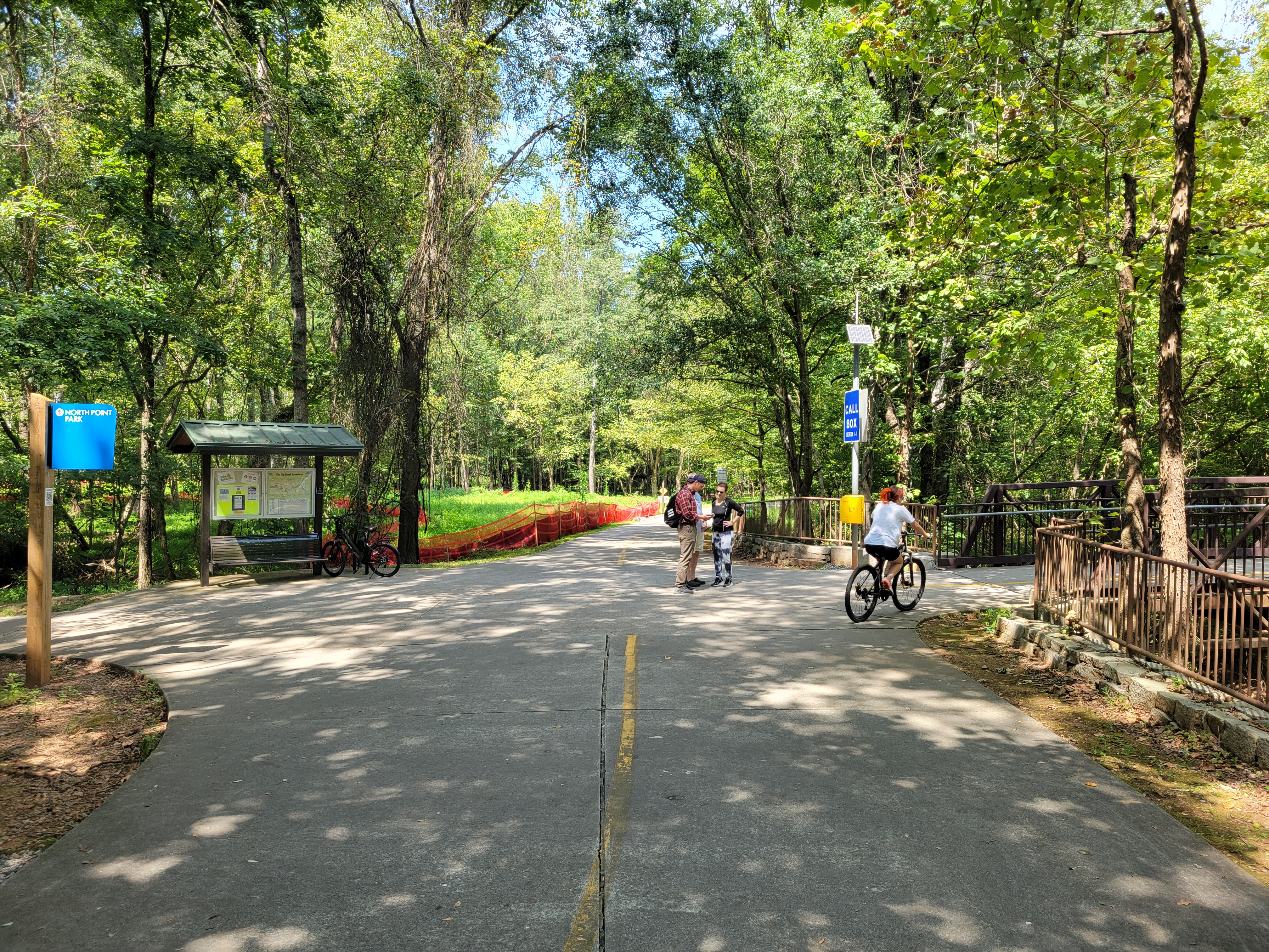 Paved greenway trail with cyclists and pedestrians under a canopy of trees.