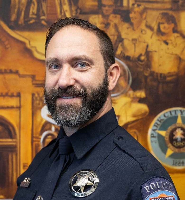 Uniformed police officer with badge and Park City seal visible in background.
