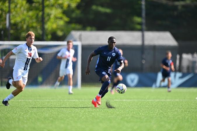 Soccer player in dark blue jersey number 11 dribbling a ball on a grass field.